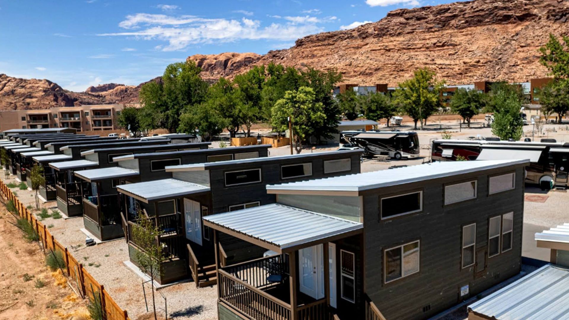 Rows of dark gray tiny homes with white roofs, set against red rocks, under a blue sky.