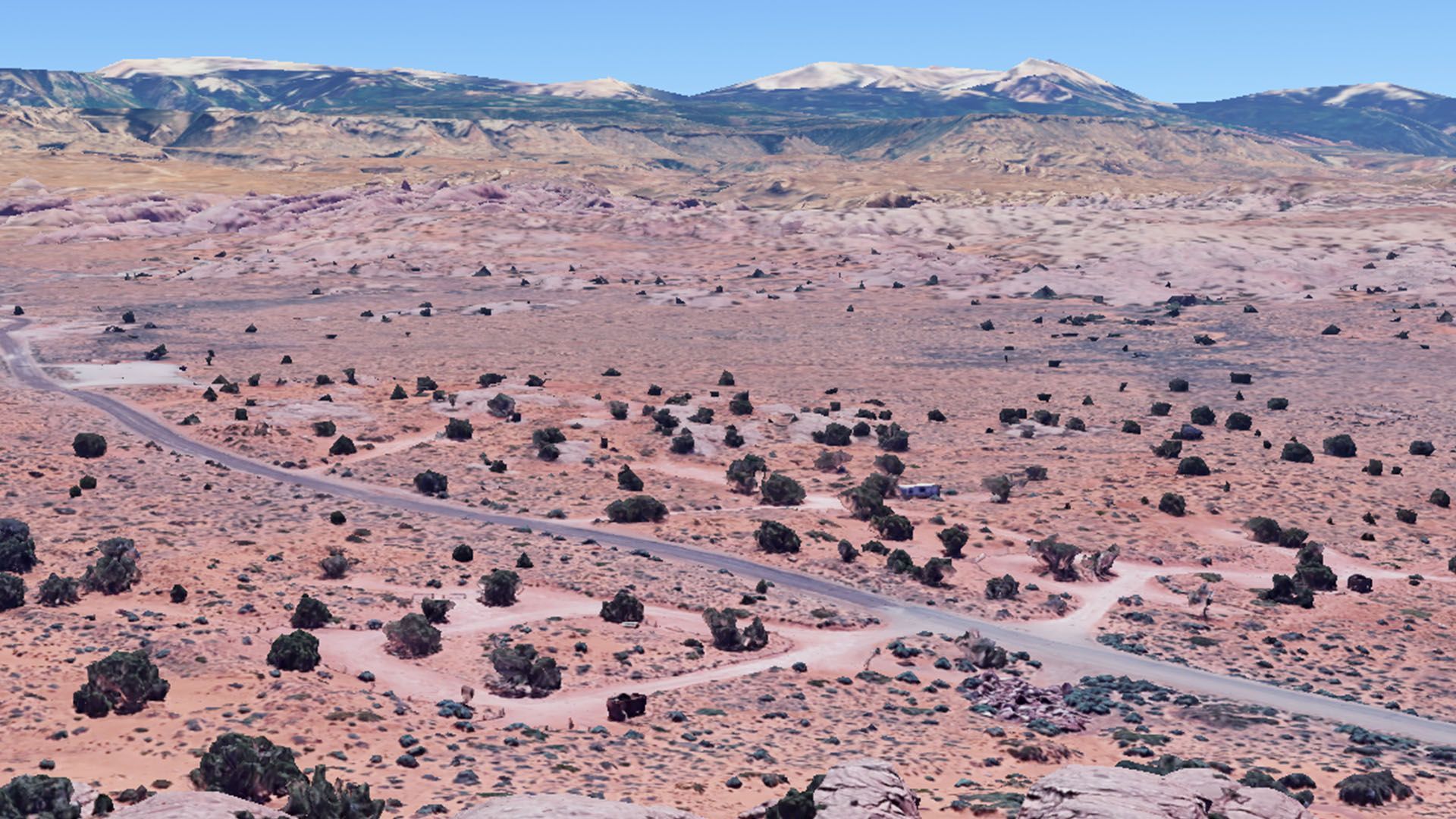 Desert landscape with campground loop road, scrub brush, and distant mountains with snow.