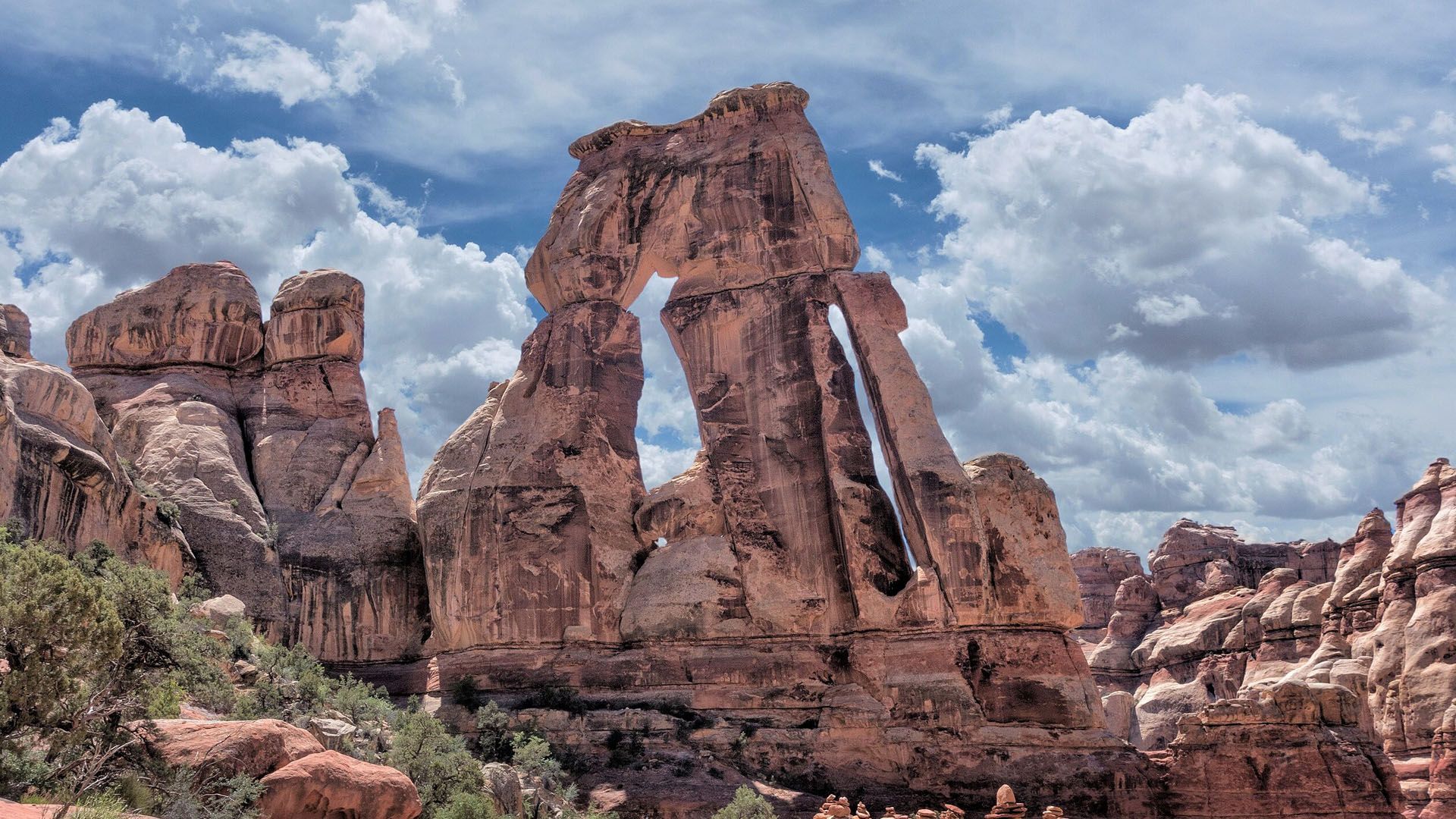Sandstone arch in a desert landscape under a partly cloudy blue sky.