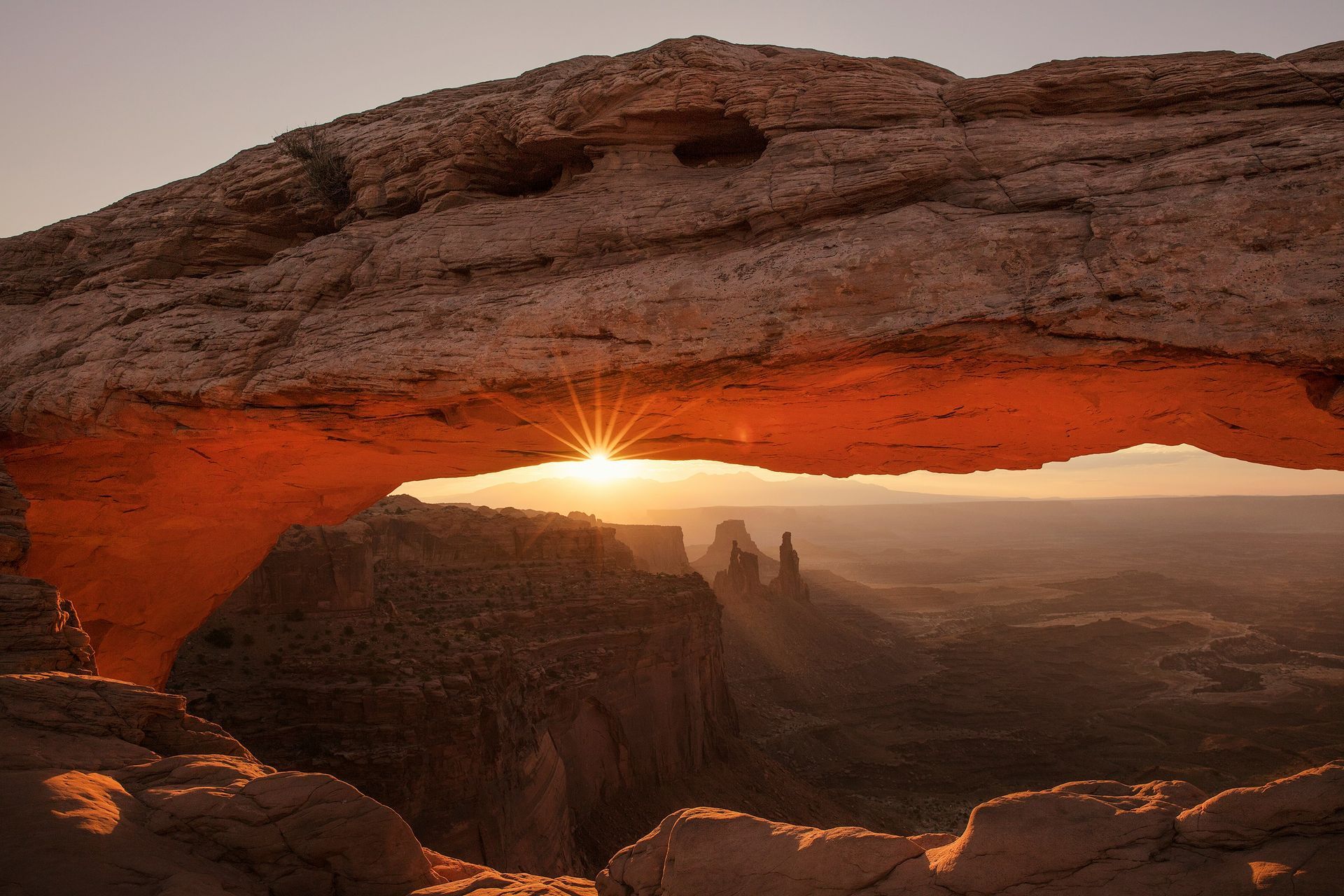 Sunrise through Mesa Arch in Canyonlands National Park, Utah. Orange rock formation frames the sun.