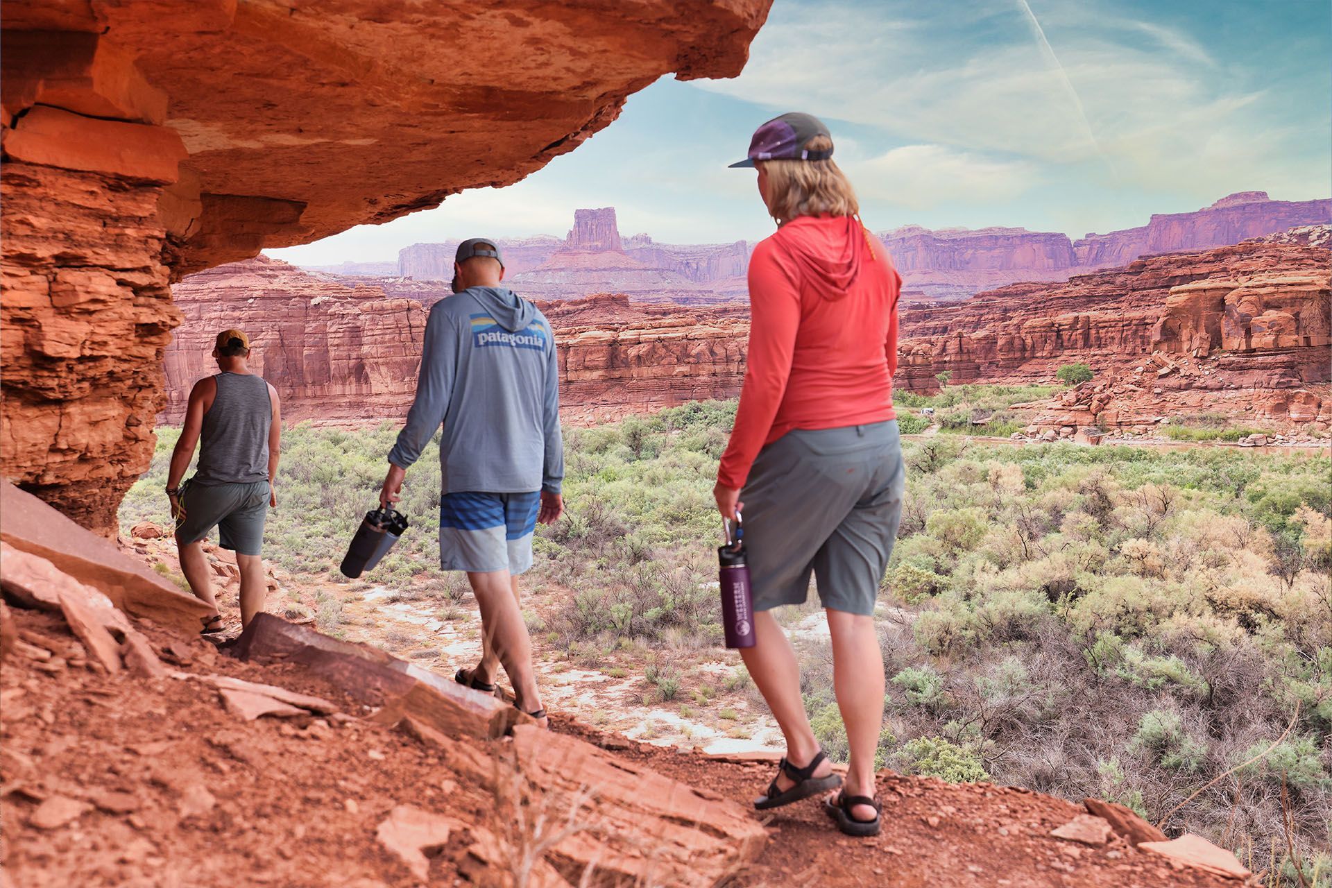 Three people hiking in a red-rock desert landscape, under a rock overhang.