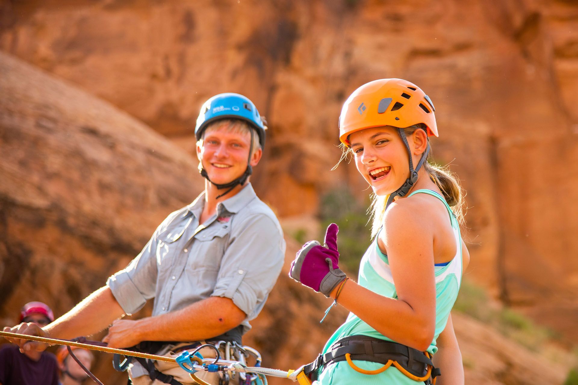 A girl in a harness gives a thumbs up.