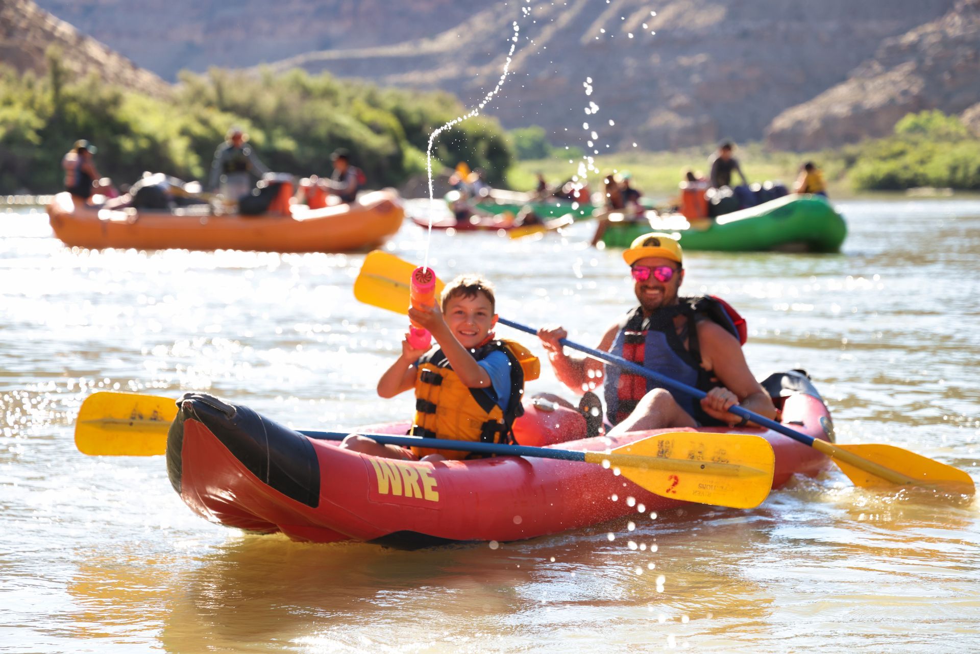 Father and son in an inflatable kayak floating on the Green River; the boy shoots water from a water squirter.