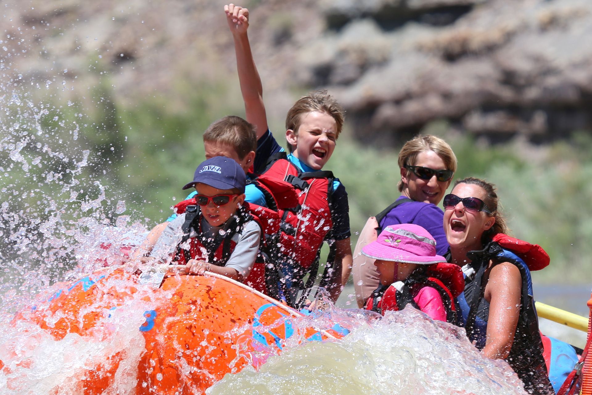 A family rafts Desolation Canyon with a boy raising his arm in excitement at the front of the raft