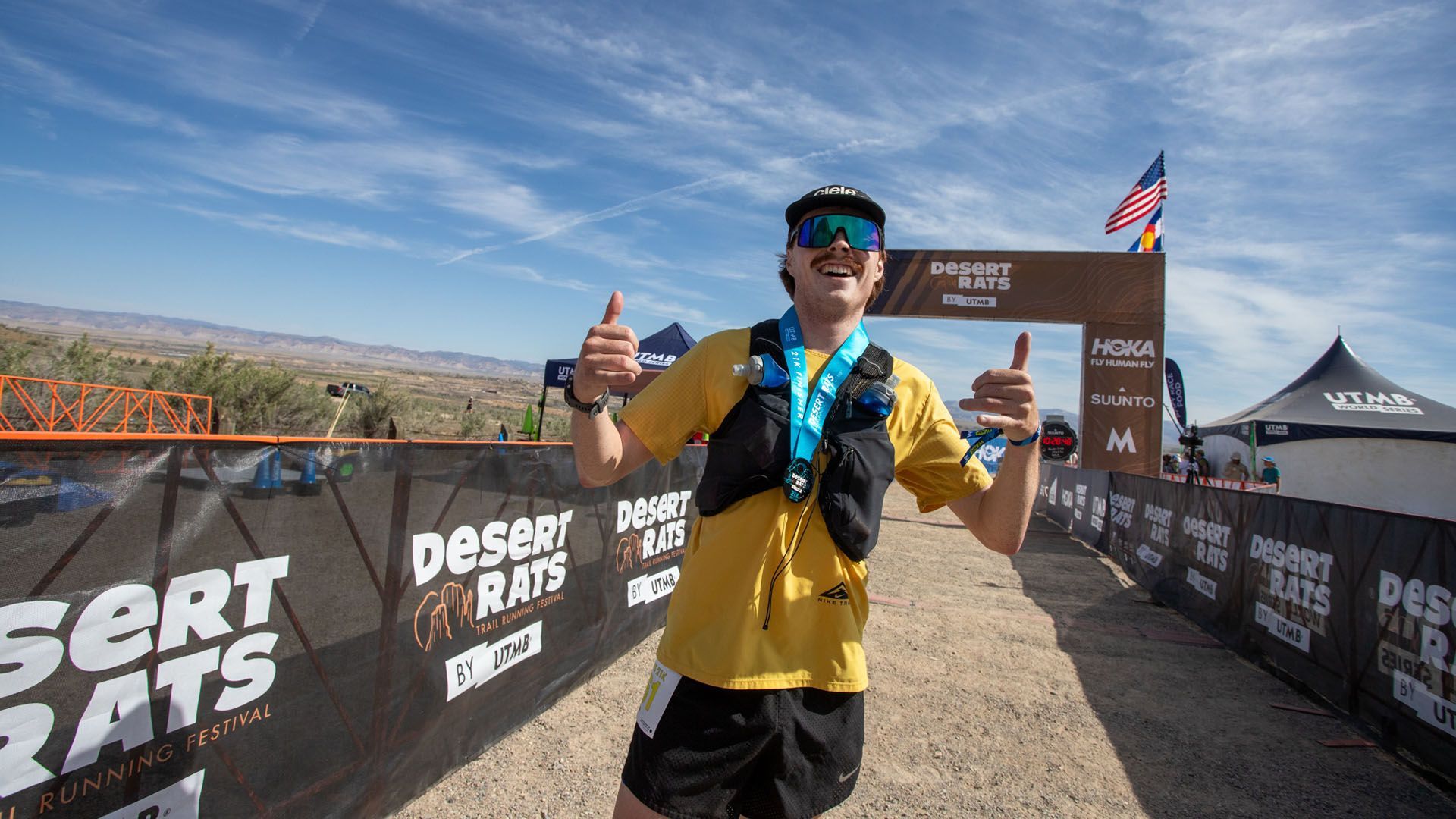 Man with medal gives thumbs up at Desert Rats race finish line.