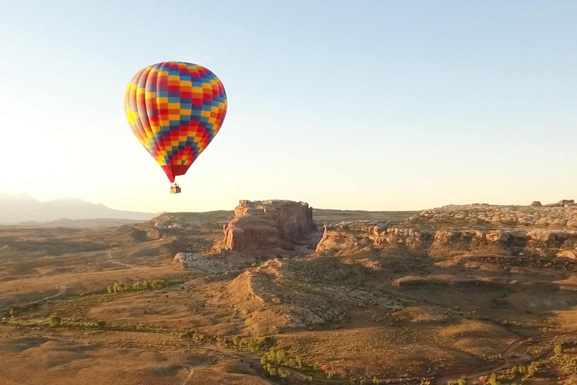 Hot air balloon over a desert landscape with red rock formations and a clear sky.