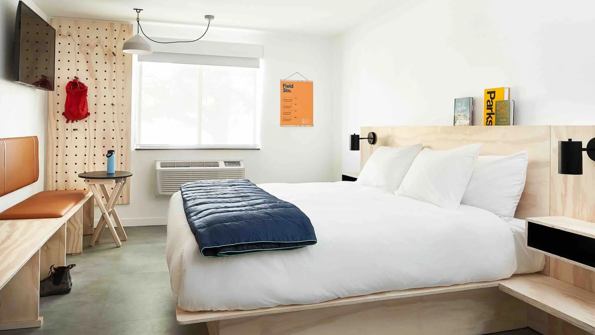 Modern hotel room with a bed, desk, and pegboard wall. Bright and minimalist.