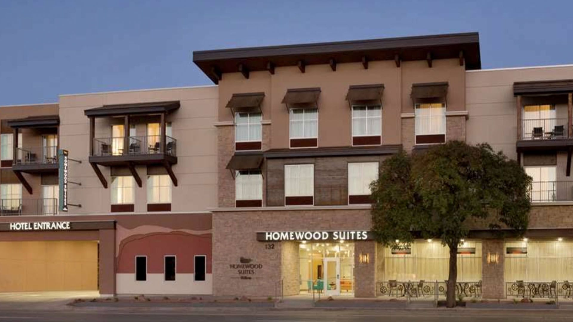 Exterior of Homewood Suites hotel at dusk, with entrance sign and open lobby.