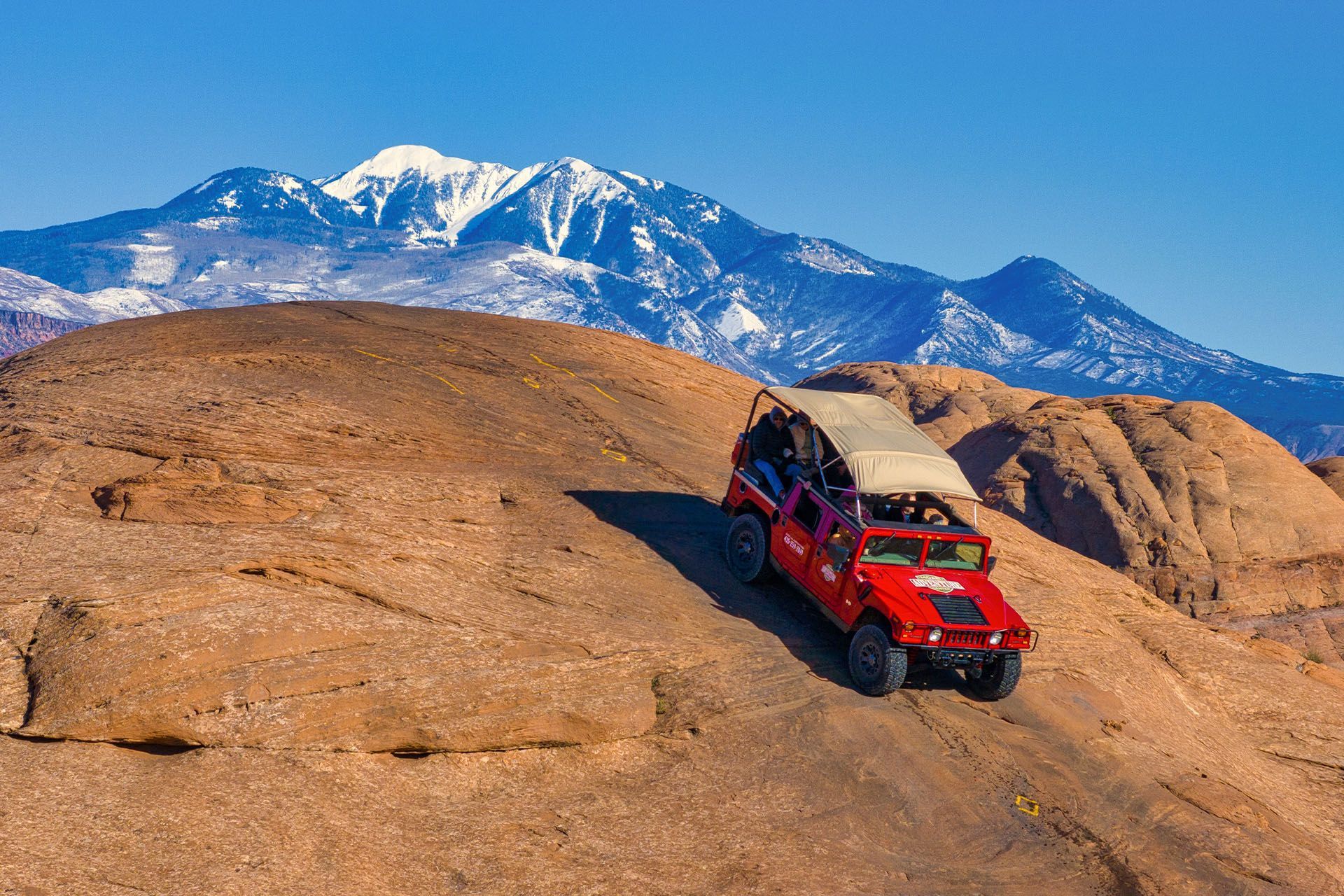 Navigating the infamous Hells Revenge Trail in Moab, Utah, in a bright red Hummer H1 off-road vehicle.