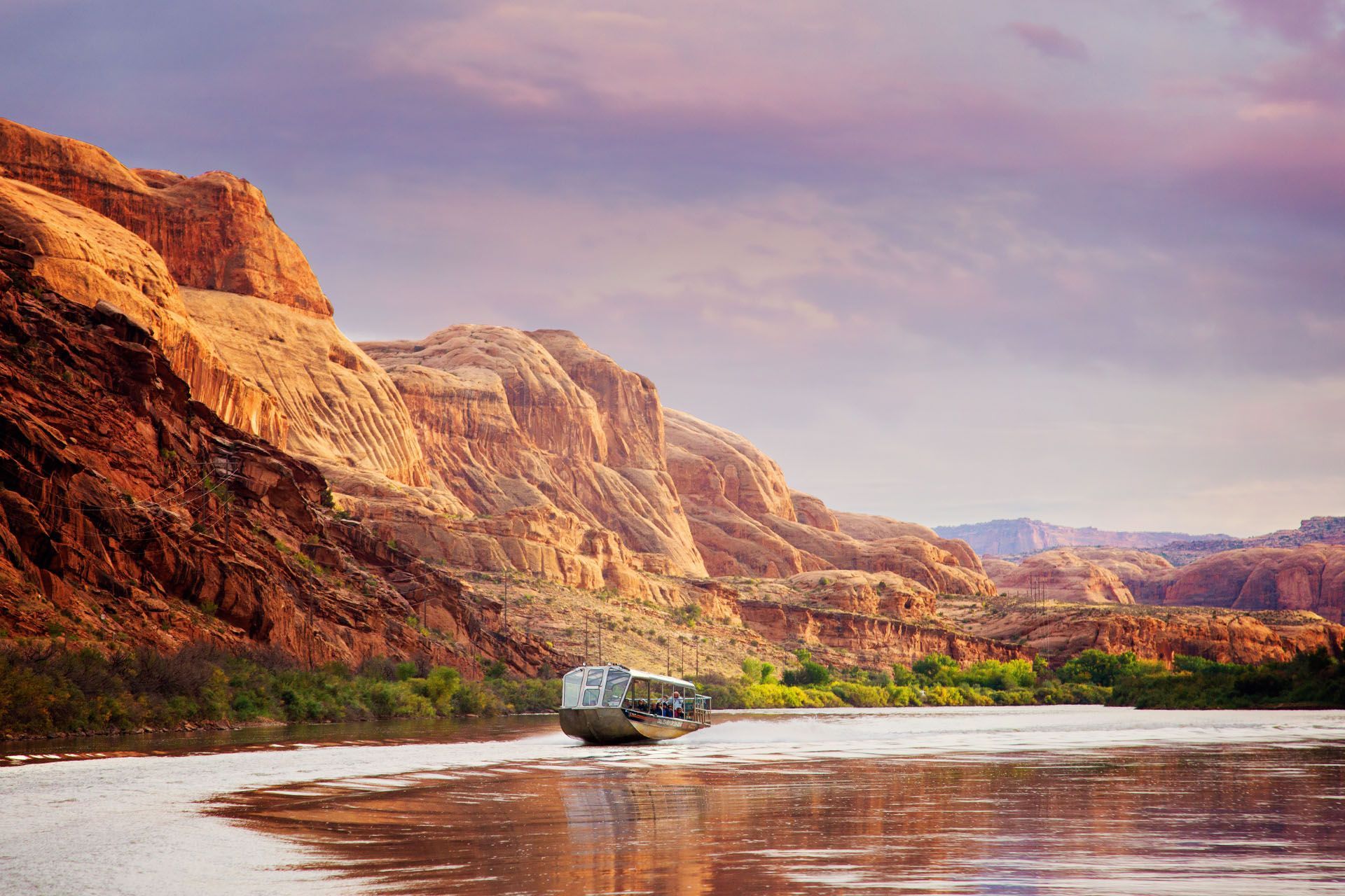 A jetboat glides down the Colorado River at sunset.