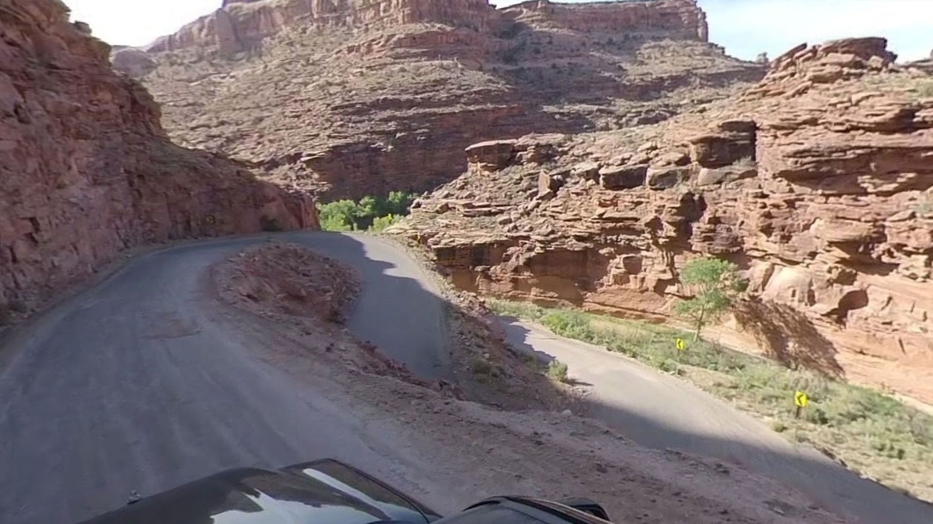 Dirt road winds through a canyon of red rock formations under a sunny sky.