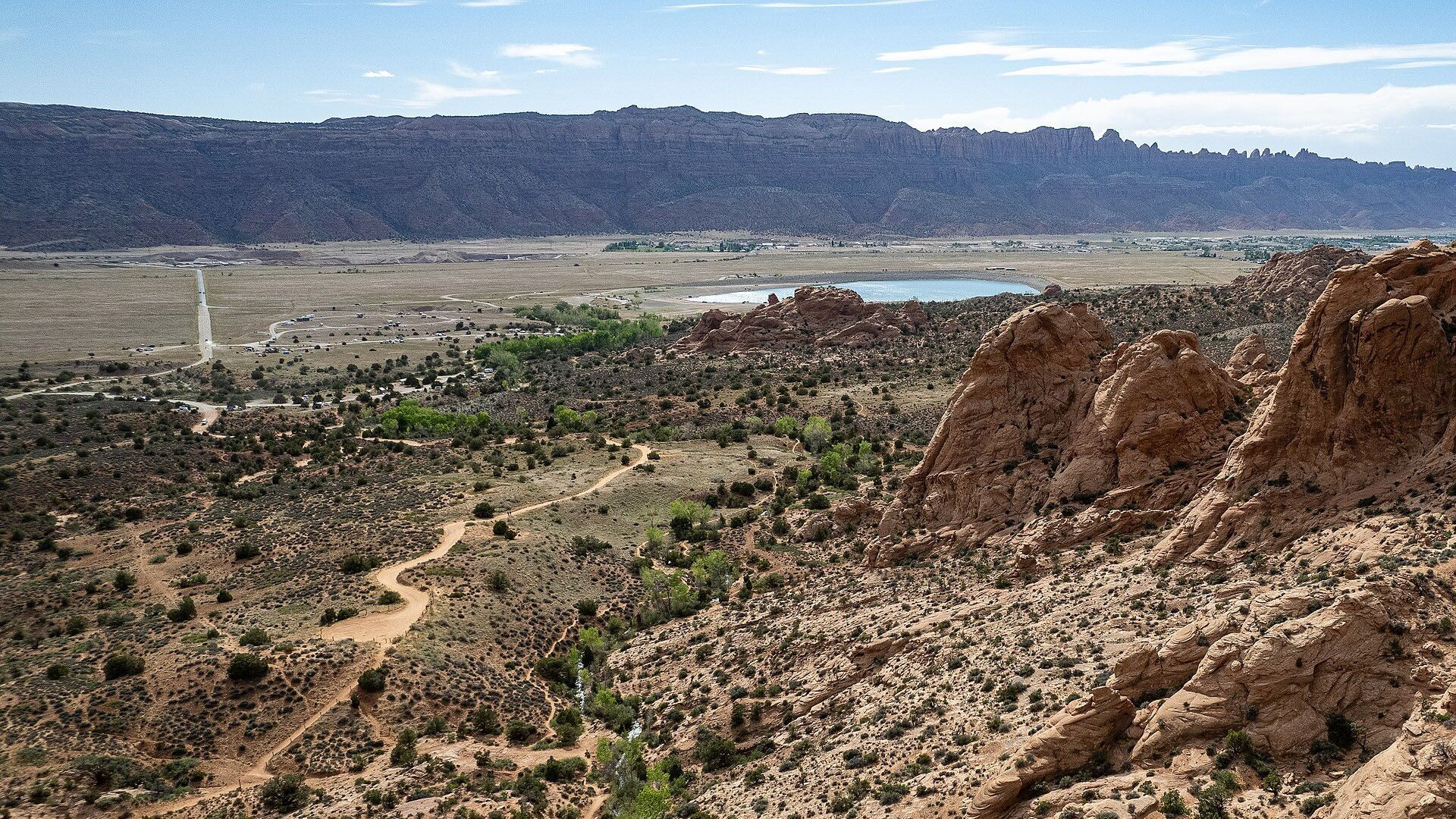 View of a desert landscape with rock formations in the foreground and mountains in the distance under a blue sky.