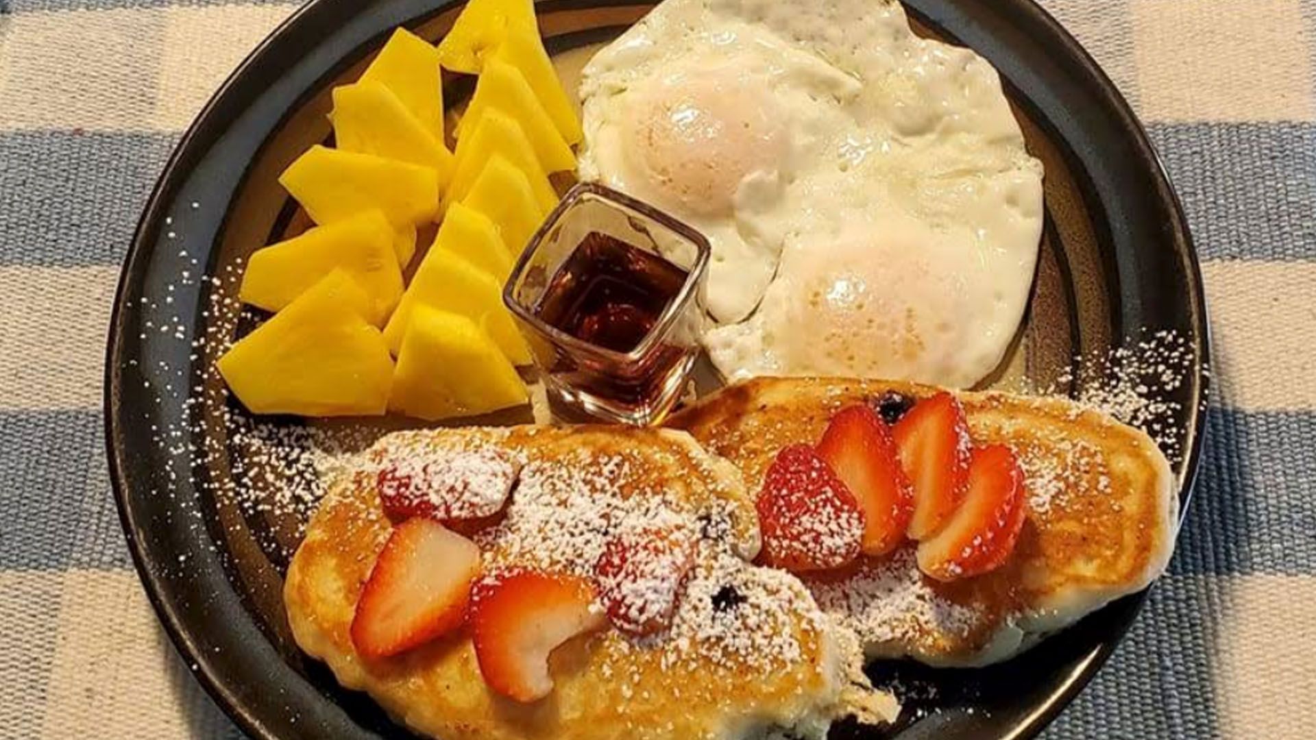 Breakfast plate: pancakes with strawberries, fried eggs, mango slices, and jam.