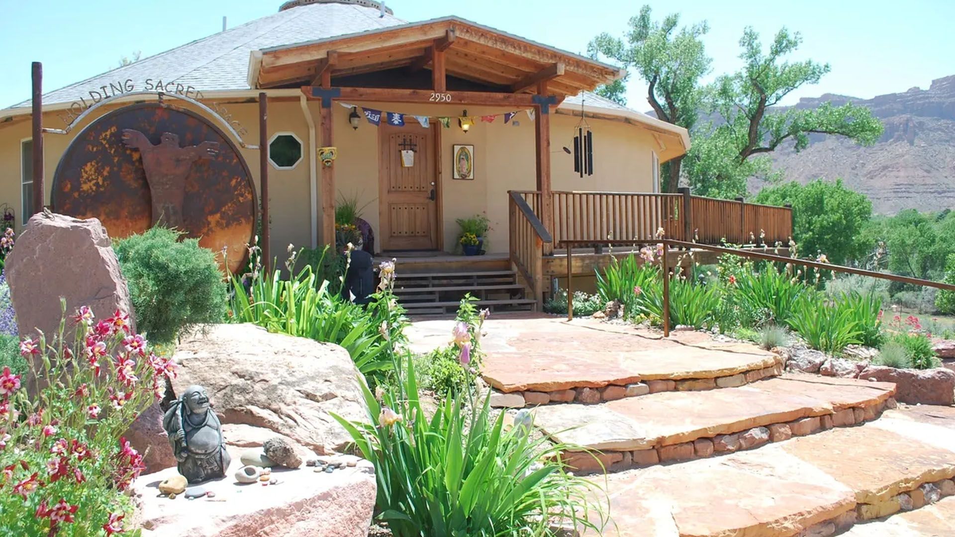 Round adobe home with wooden porch, stone steps, and desert landscaping.