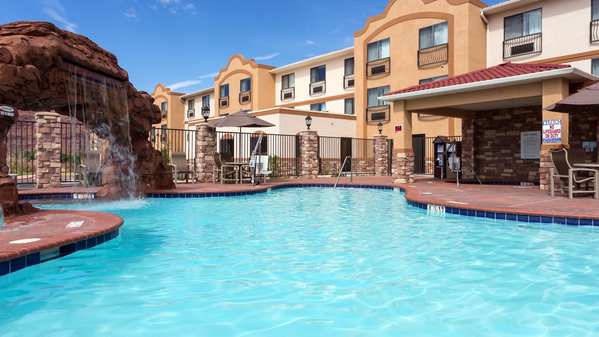 Swimming pool at a hotel with a rock waterfall feature and lounge chairs.