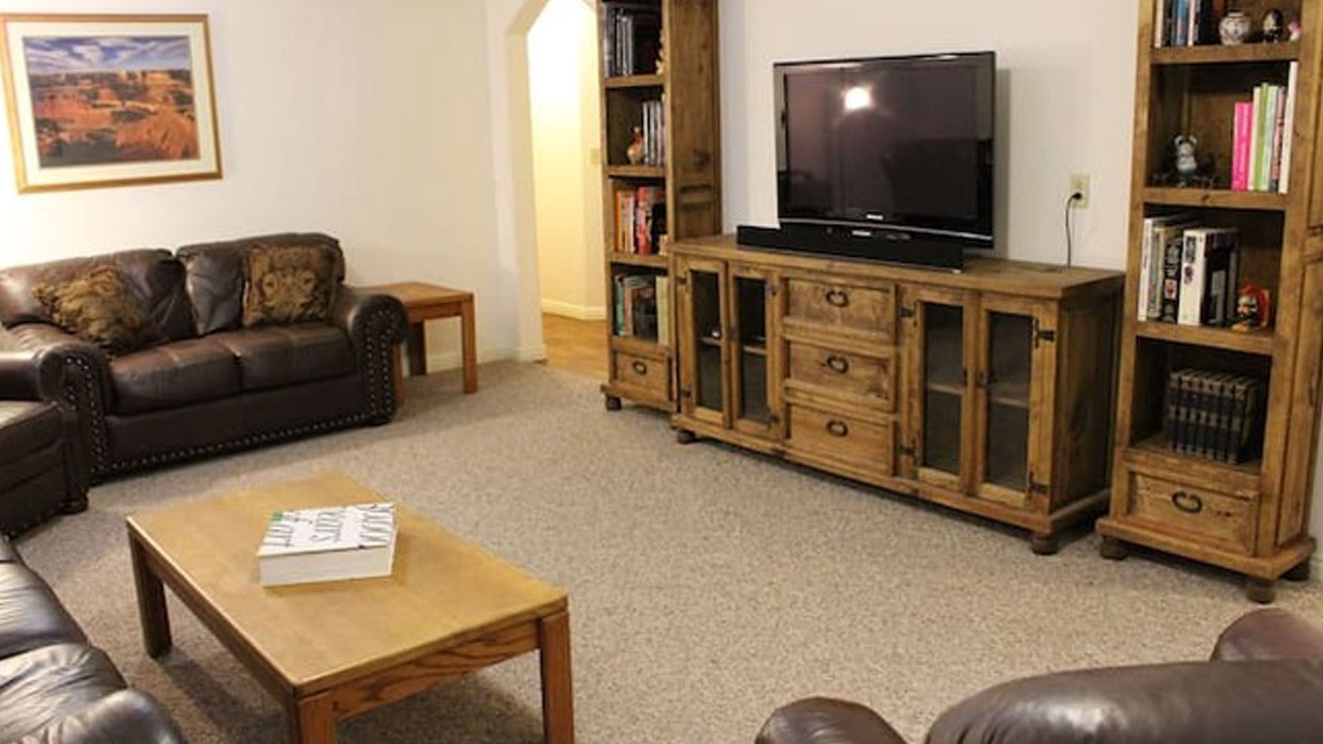 Living room with leather sofa, wooden entertainment center with TV, and carpet.