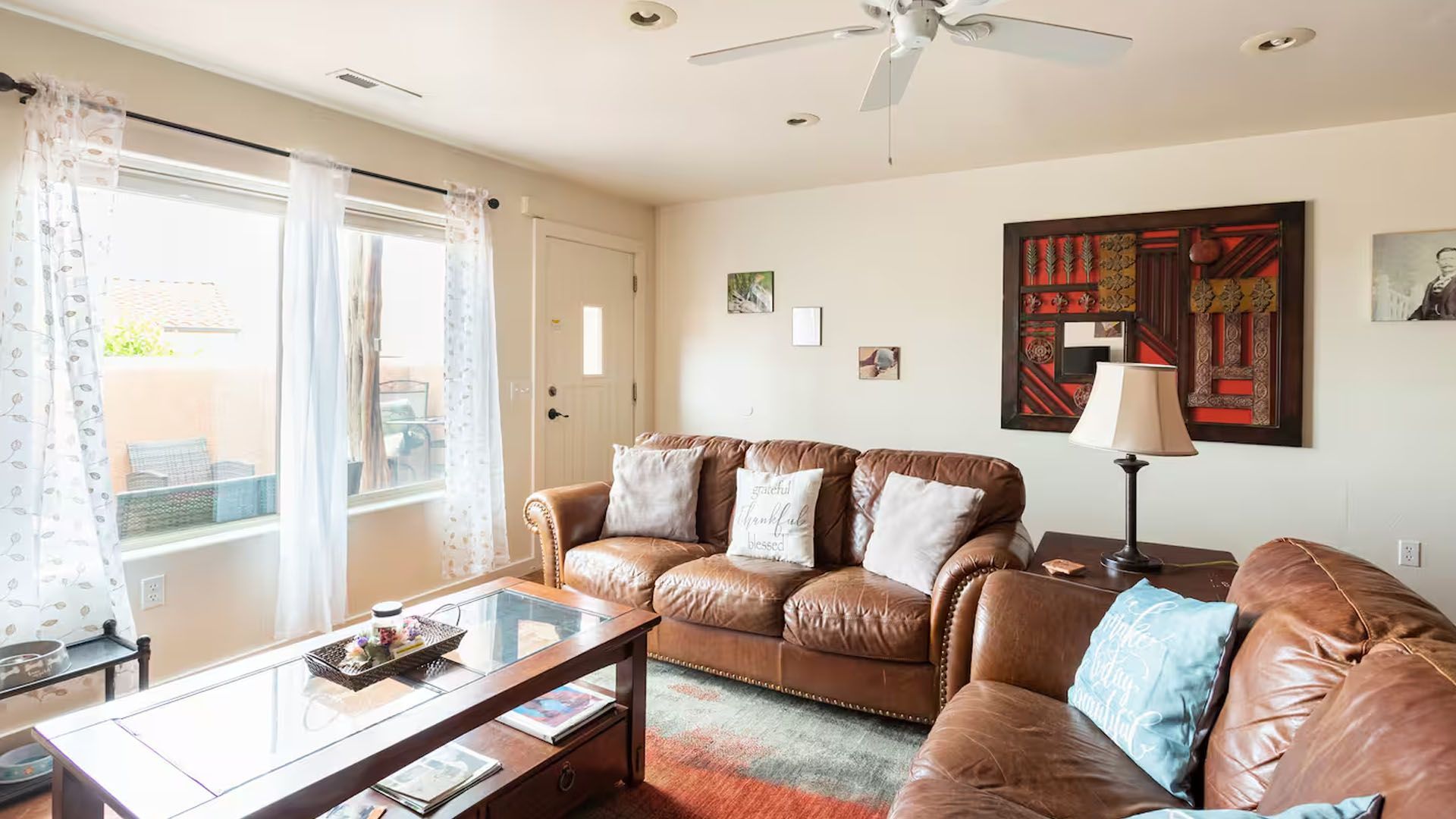 Living room with a brown leather sofa, coffee table, and large window with white curtains.