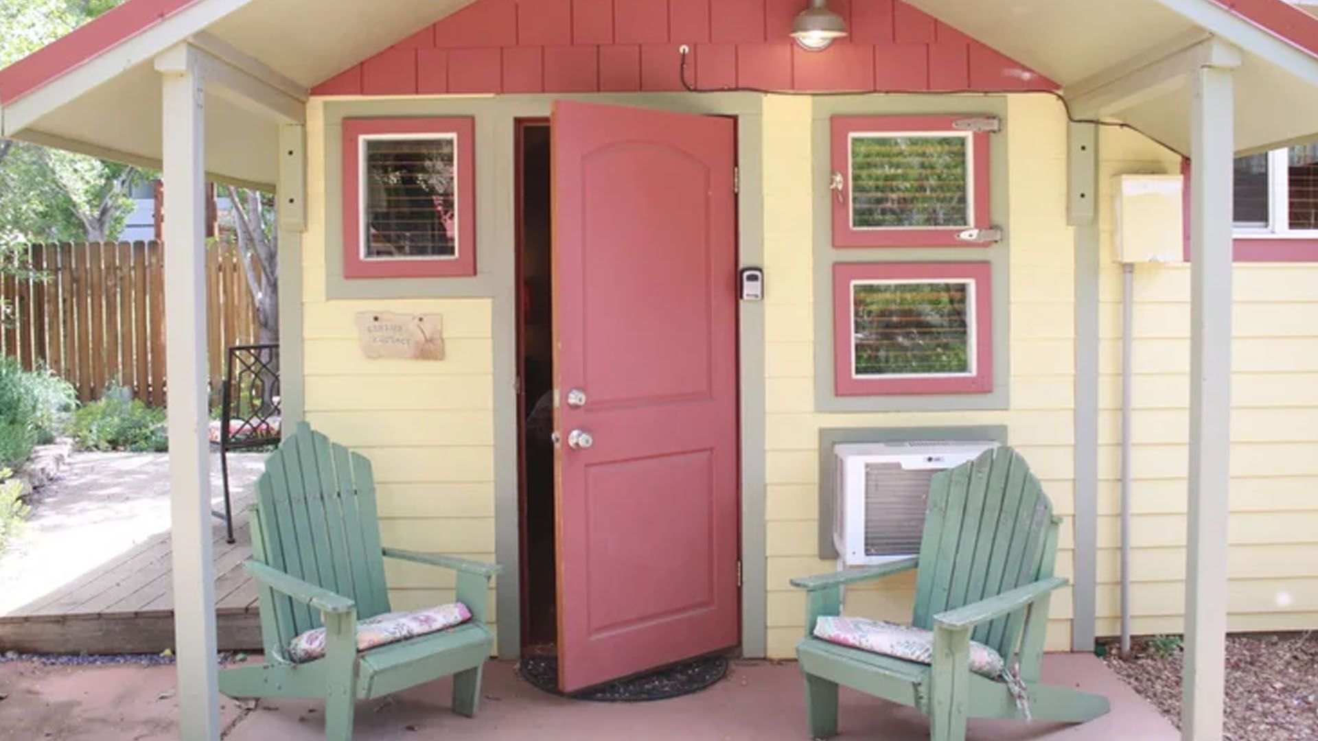 Yellow building with red trim, open red door, two green chairs on patio.