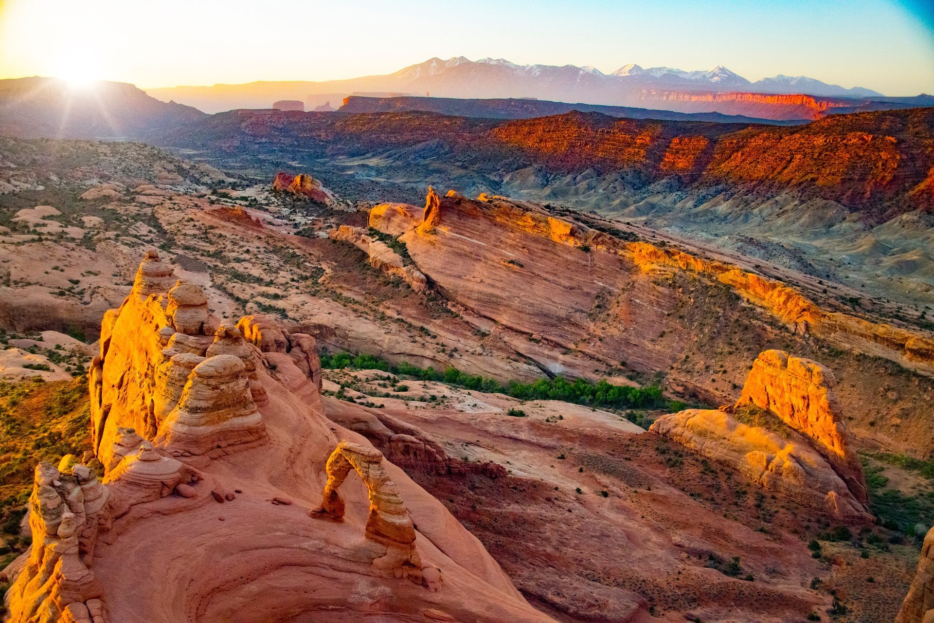The sun is setting over a desert landscape with mountains in the background.