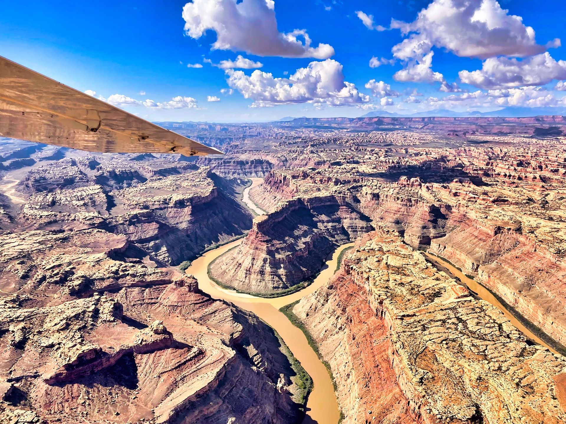 Overhead view of a canyon with a river winding through it, under a blue sky with fluffy clouds.