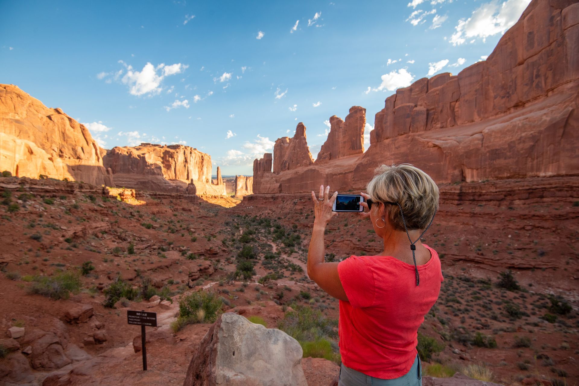 Woman taking photo of red rock landscape with smartphone.