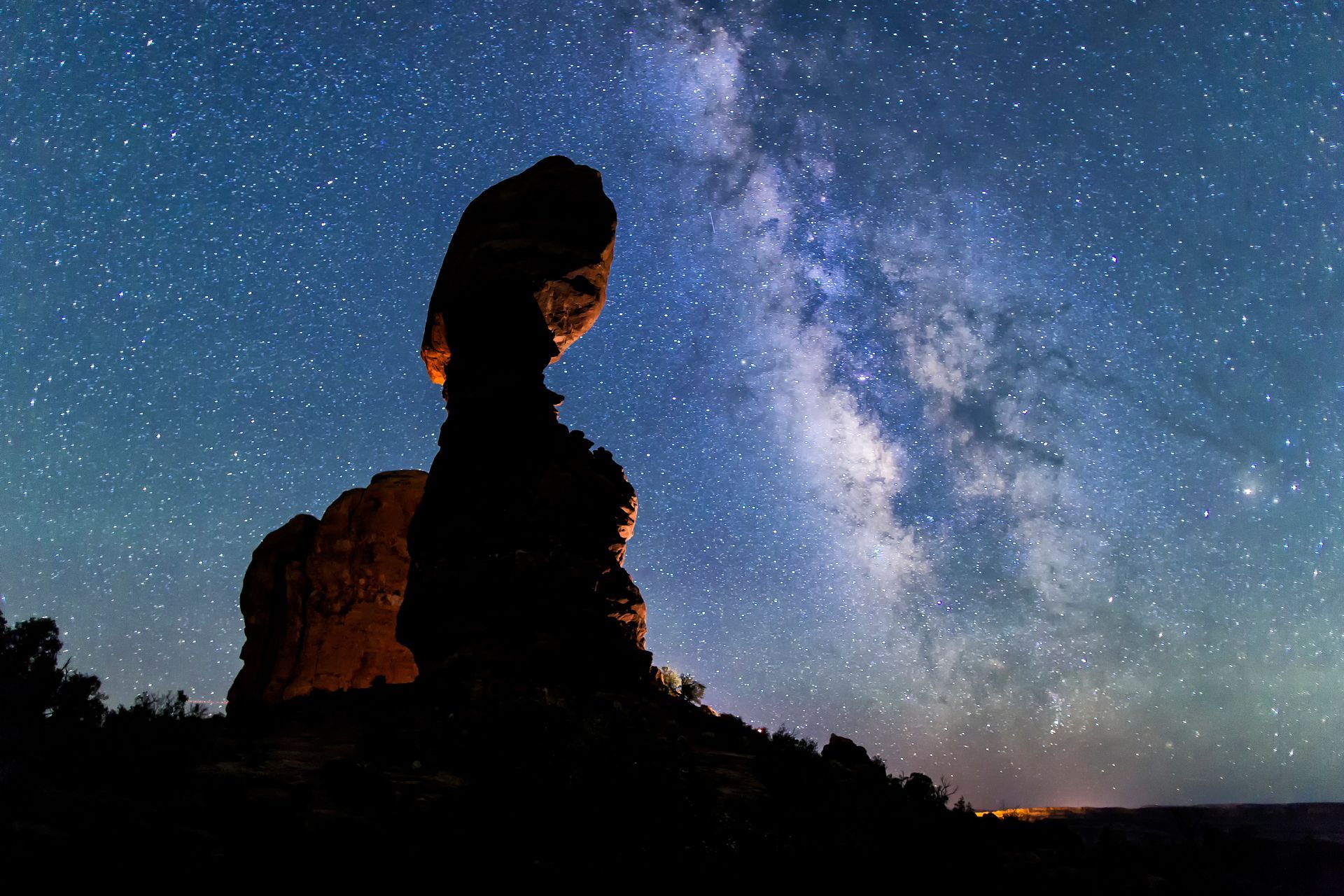 Silhouette of Balanced Rock in Arches National Park under the Milky Way in a dark night sky.