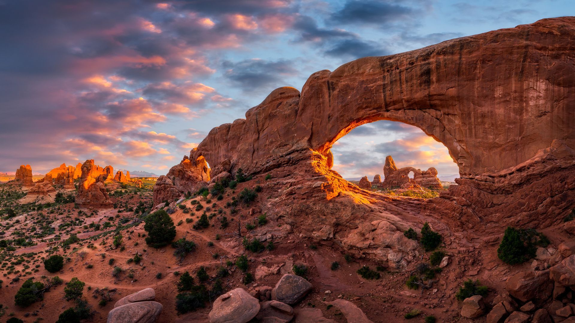 Sunset through North Window Arch in Arches National Park, Utah. Orange and blue sky, desert landscape.