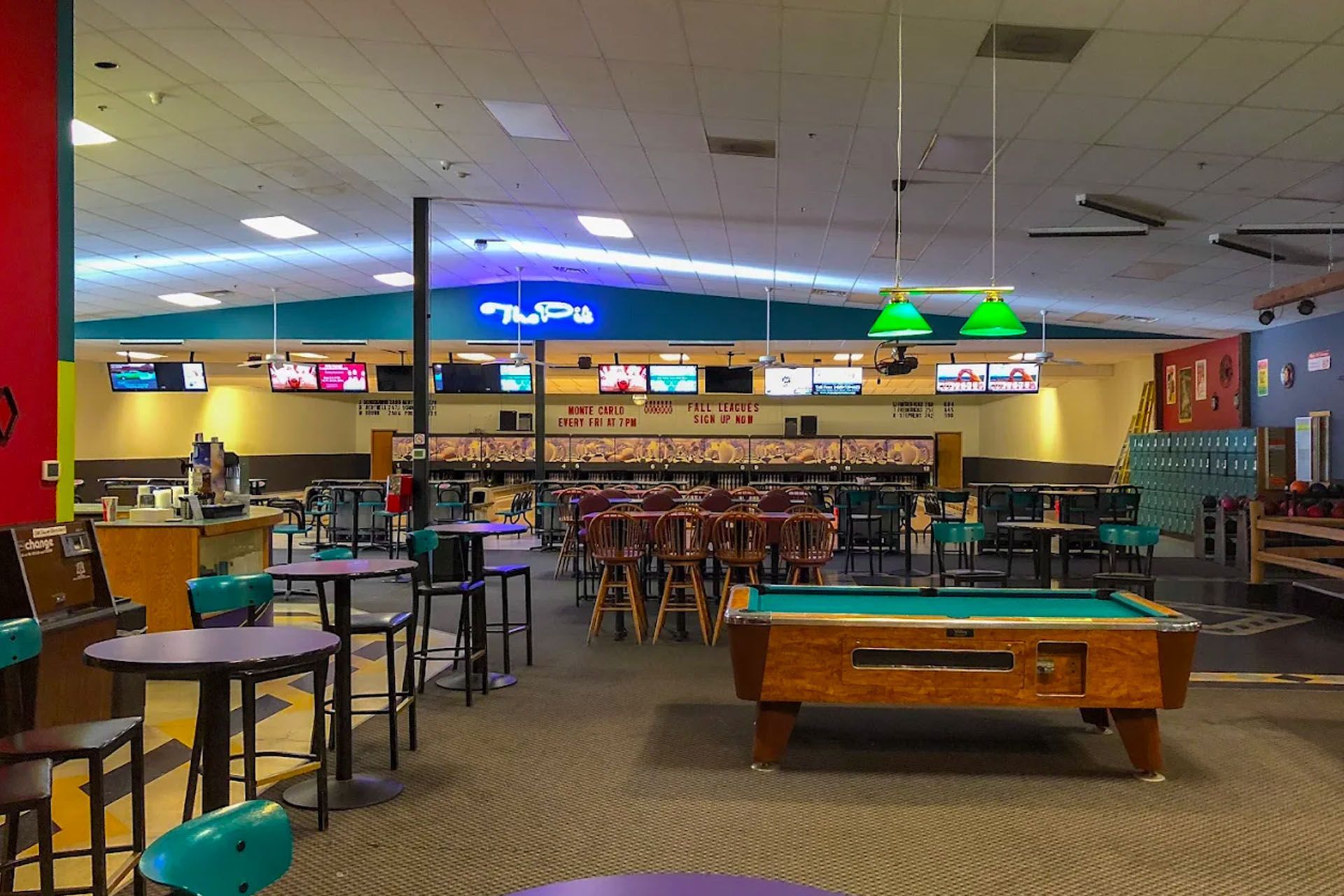 Interior of a bowling alley with tables, a pool table, and bowling lanes in the background.