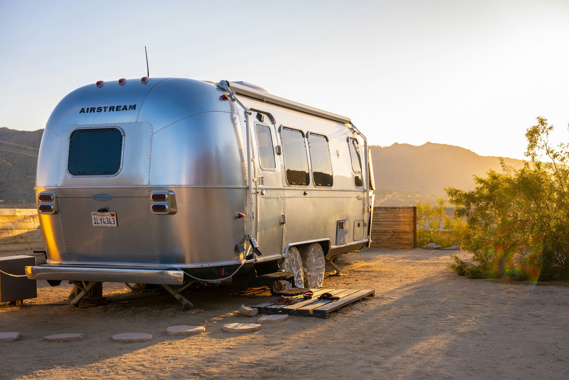 Silver Airstream trailer parked in a Moab campsite during sunset, surrounded by dry vegetation and mountains.