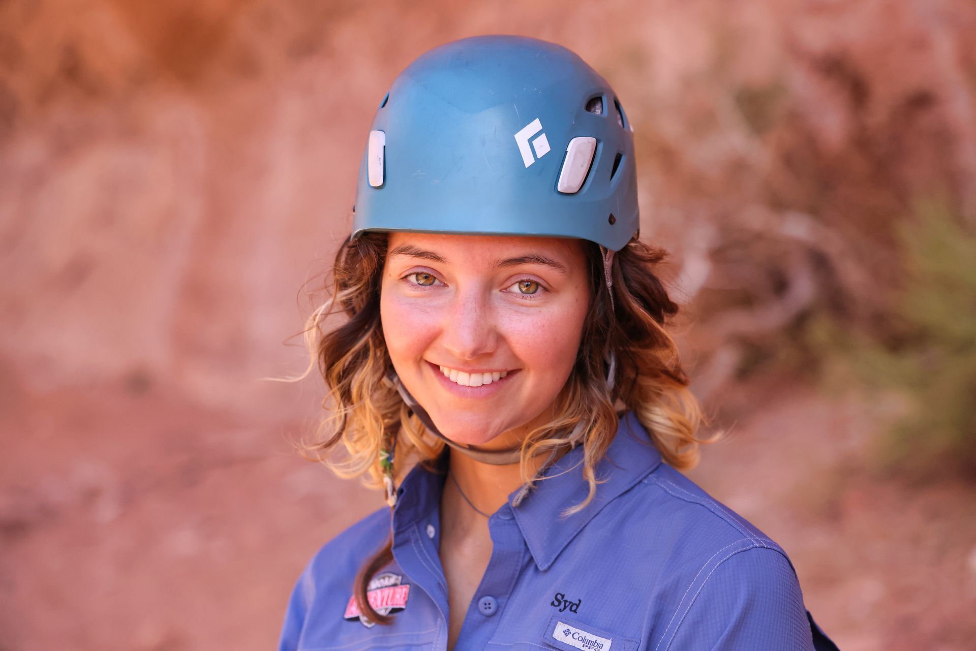 Woman canyoneering guide with teal climbing helmet smiles outdoors.