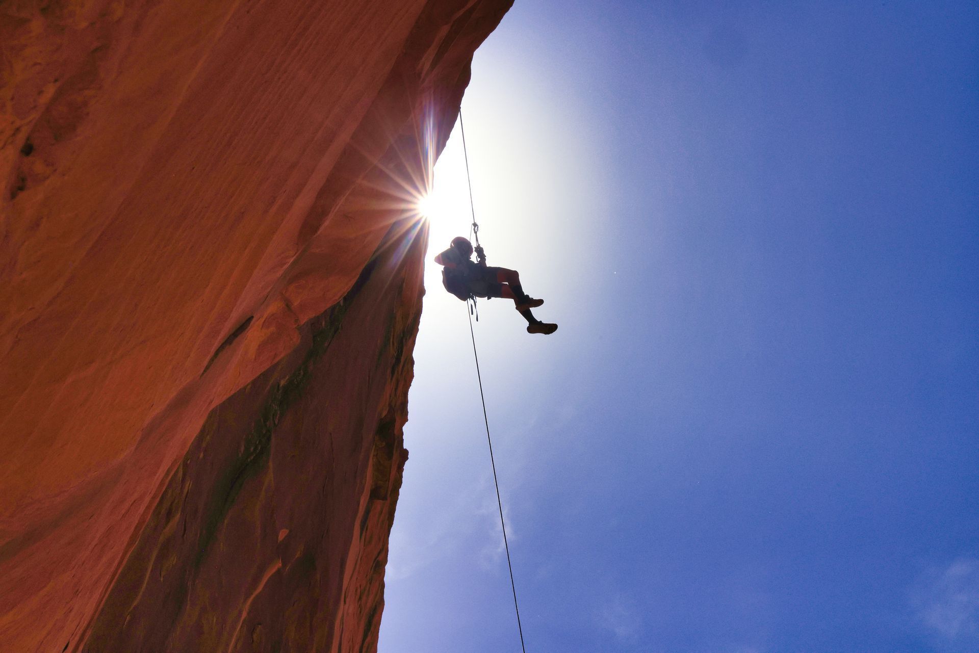 A person is rapelling from a cliff with the sun behind them.