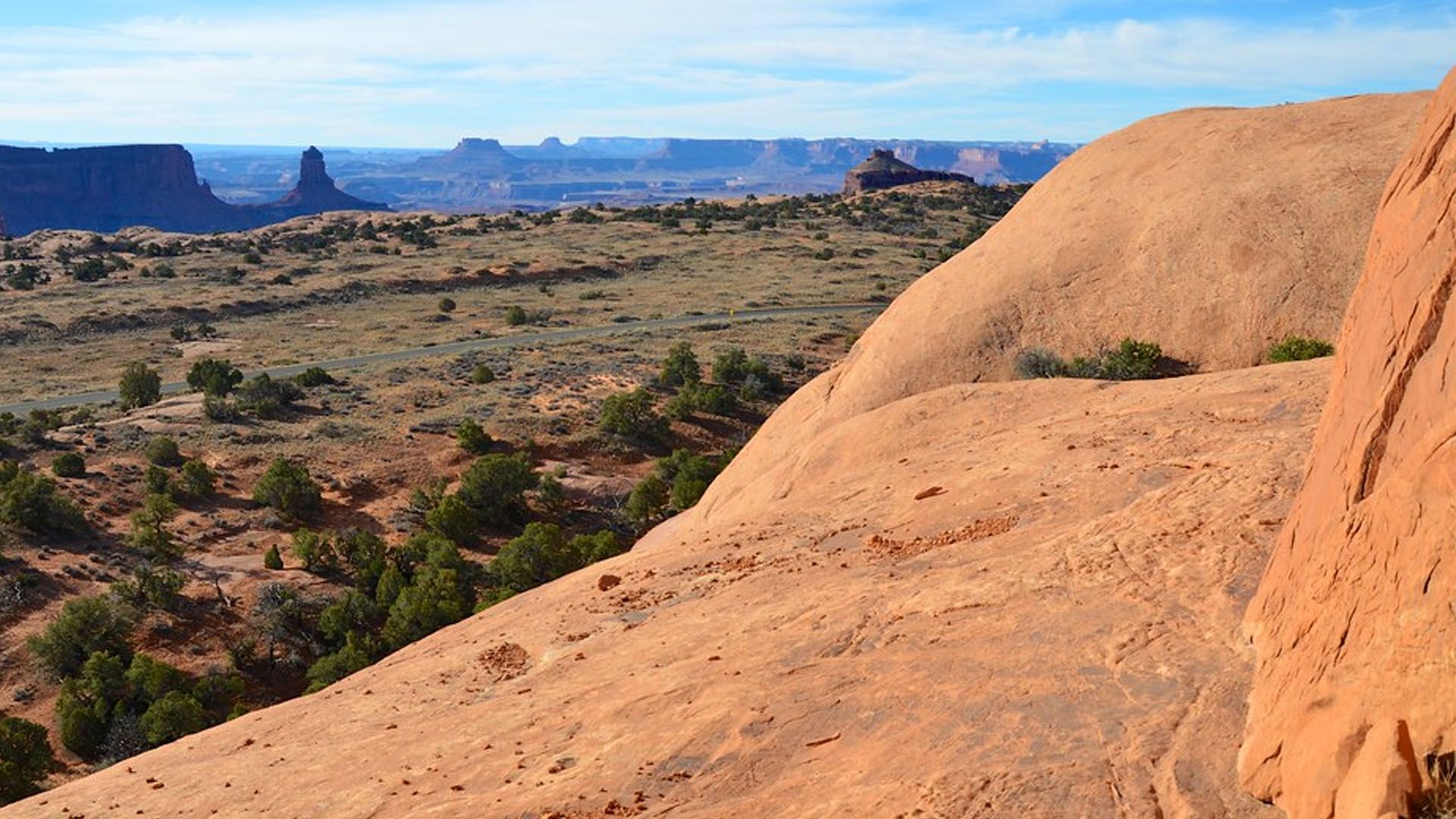 Red sandstone formations overlook a desert landscape with mesas in the distance.