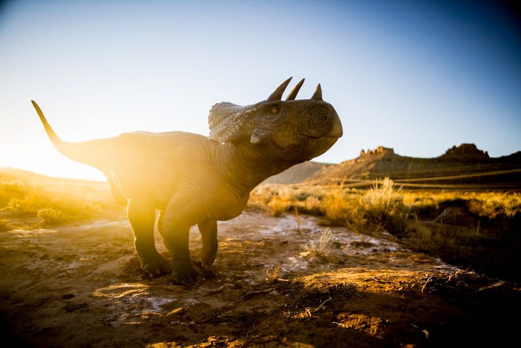 Styracosaurus dinosaur silhouette, sunlit in a dry, open landscape, with mountains in the background.