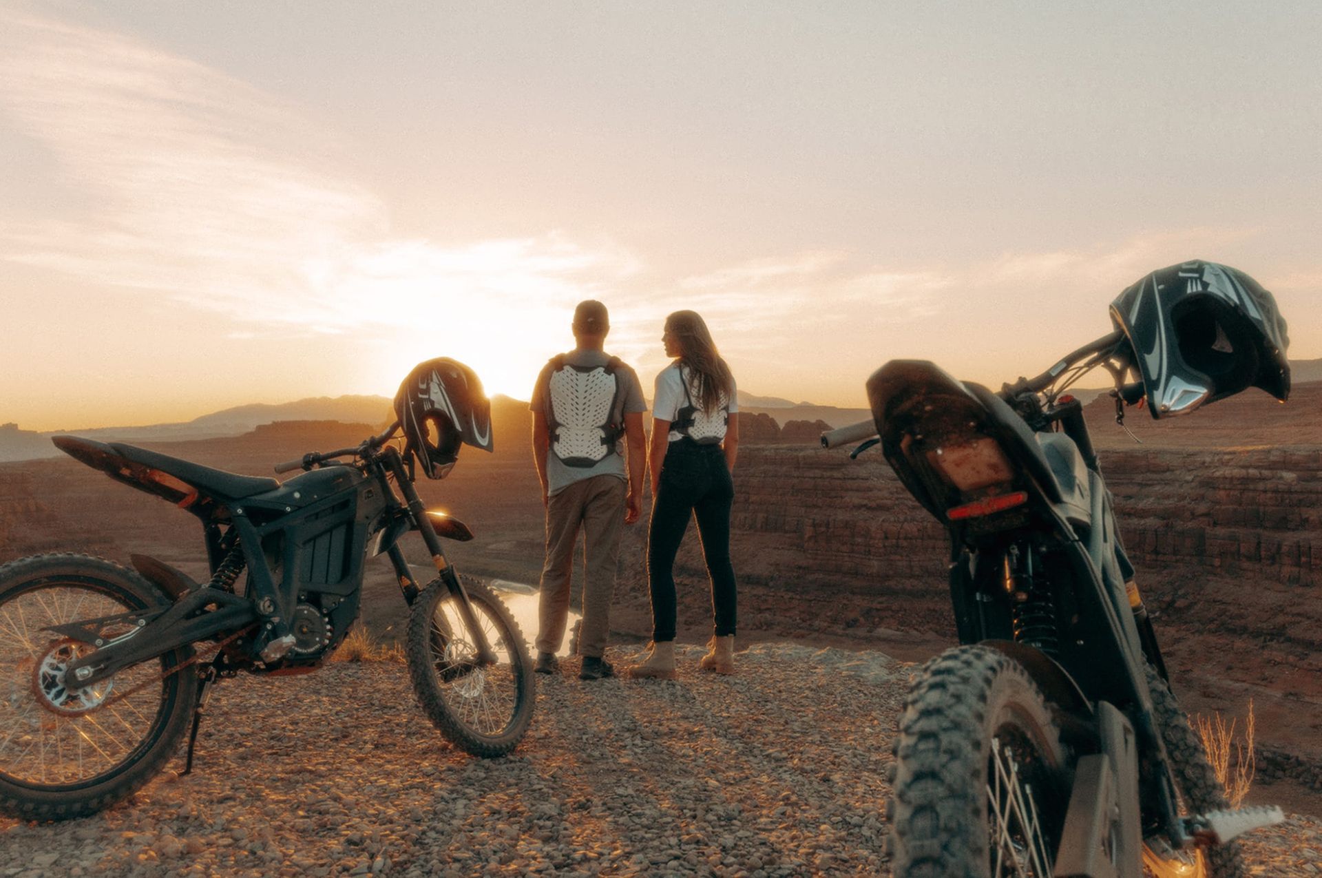 Couple admires sunset over desert landscape, flanked by electric dirt bikes.