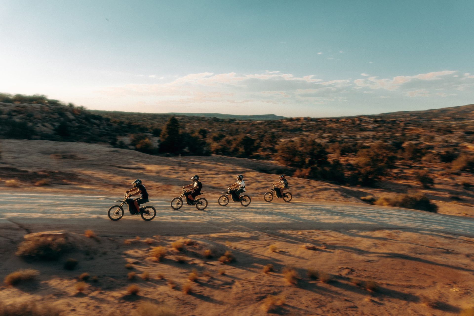 A group rides e dirt bikes through a desert landscape near Gemini Bridges.