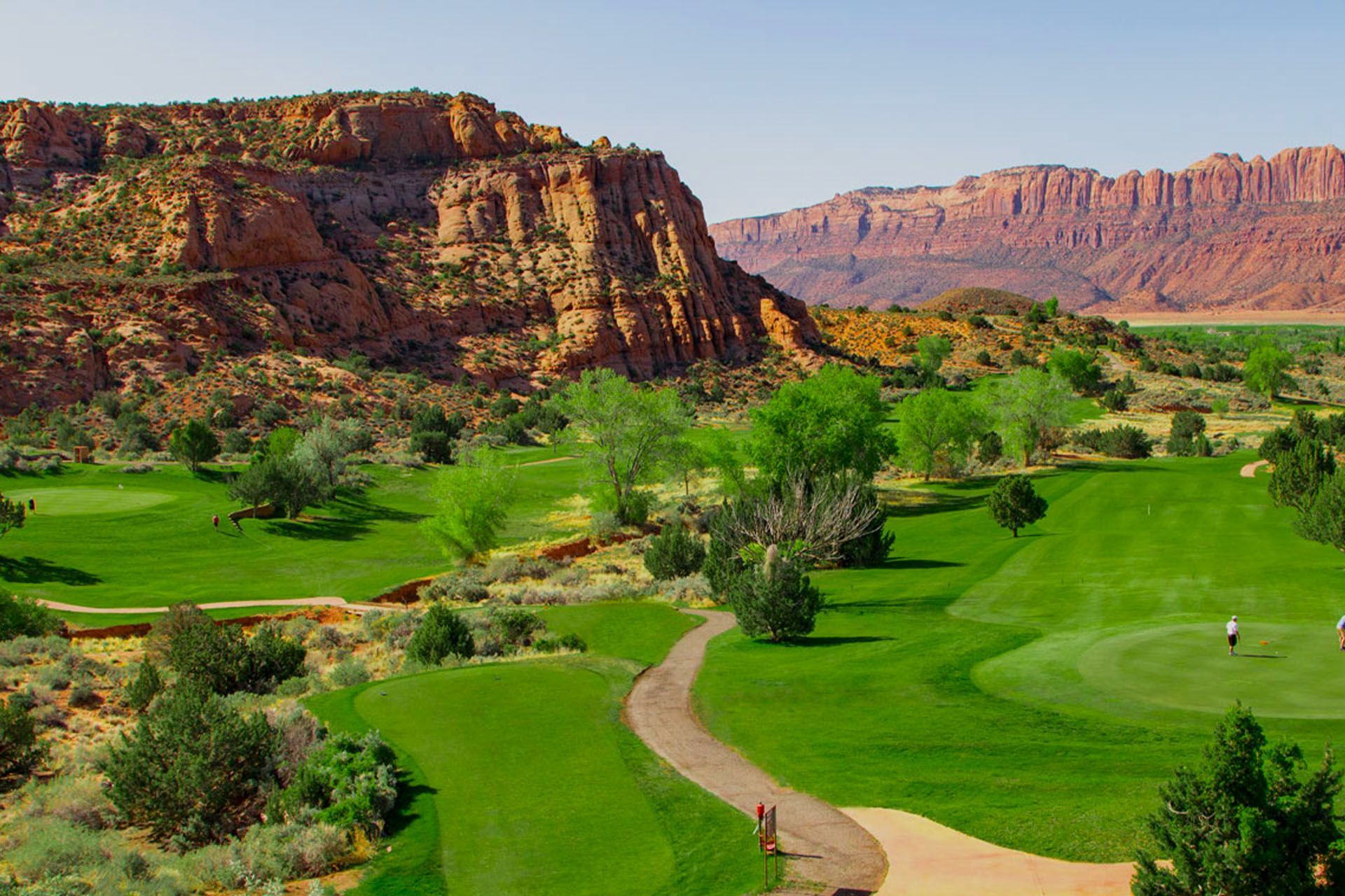 Green golf course with Moab's red rock cliffs in the background on a sunny day.