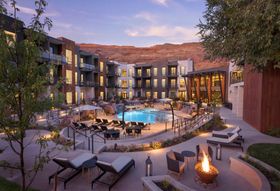 Moab resort courtyard with pool, lounge chairs, fire pit, and buildings under dusk sky.