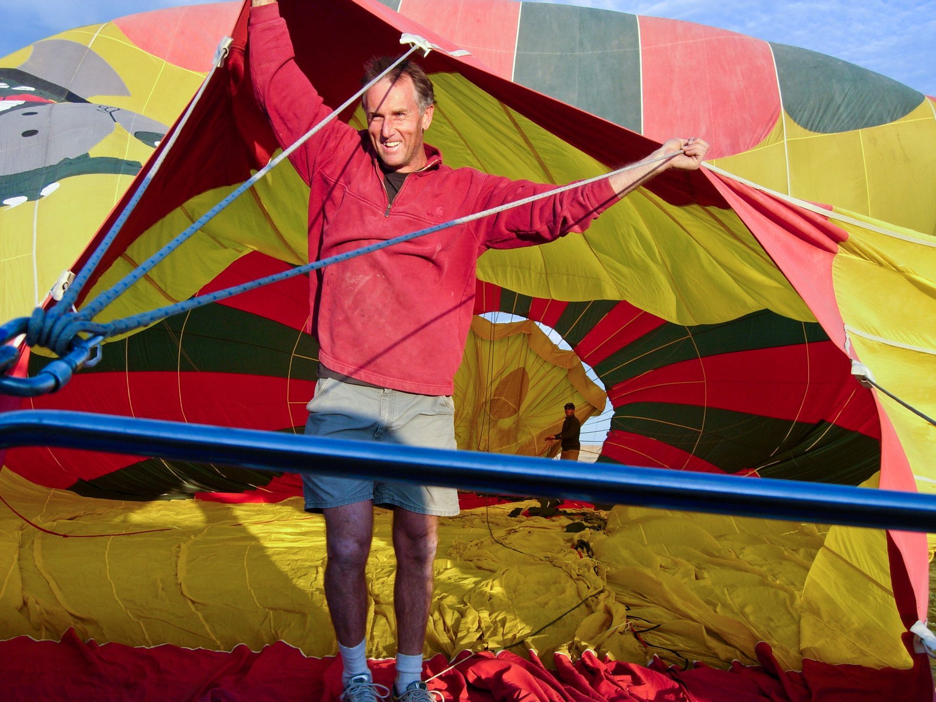 Man inside colorful hot air balloon, holding it open, smiling.