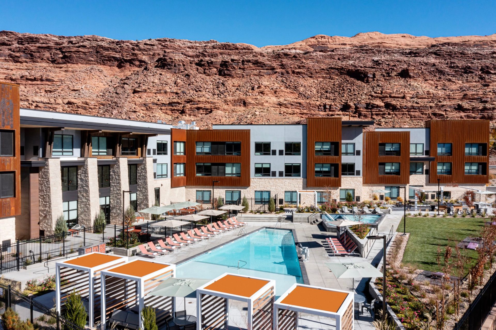 Modern hotel with pool, lounge chairs, and mountain backdrop on a sunny day.