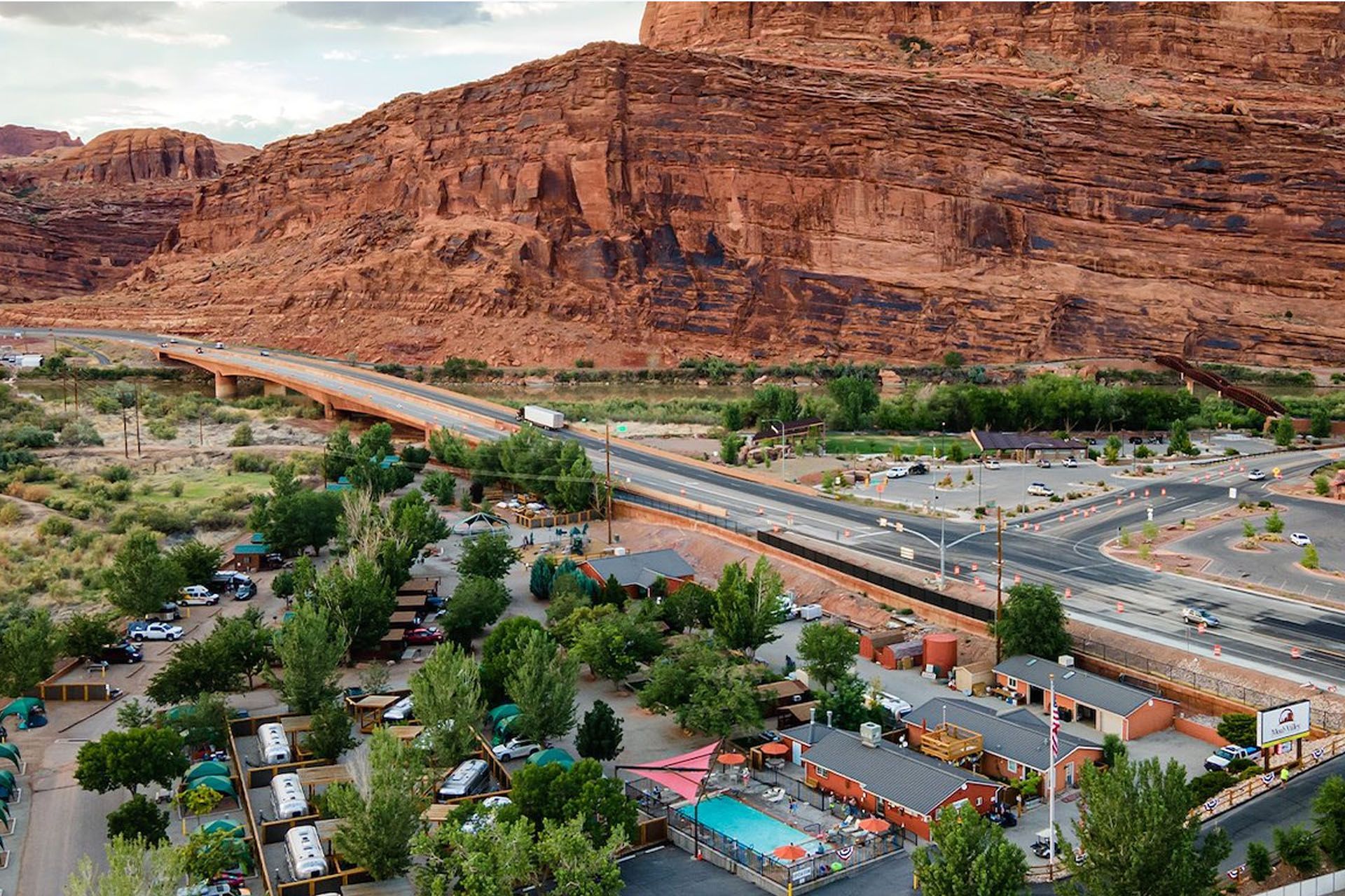 Aerial view of a campsite and road, with red rock mountain backdrop and river.