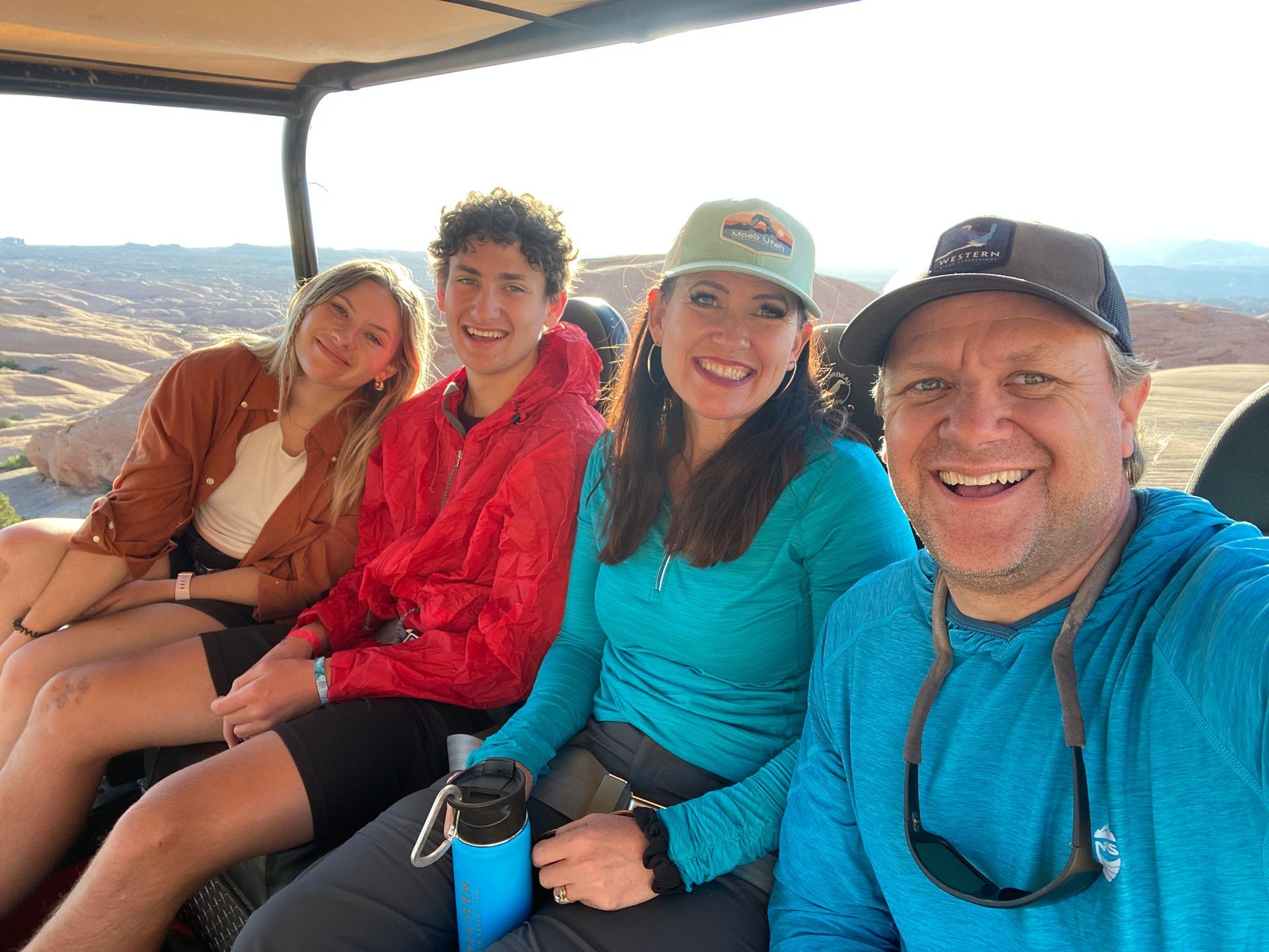 Family smiles in a golf cart outdoors, sunny day.