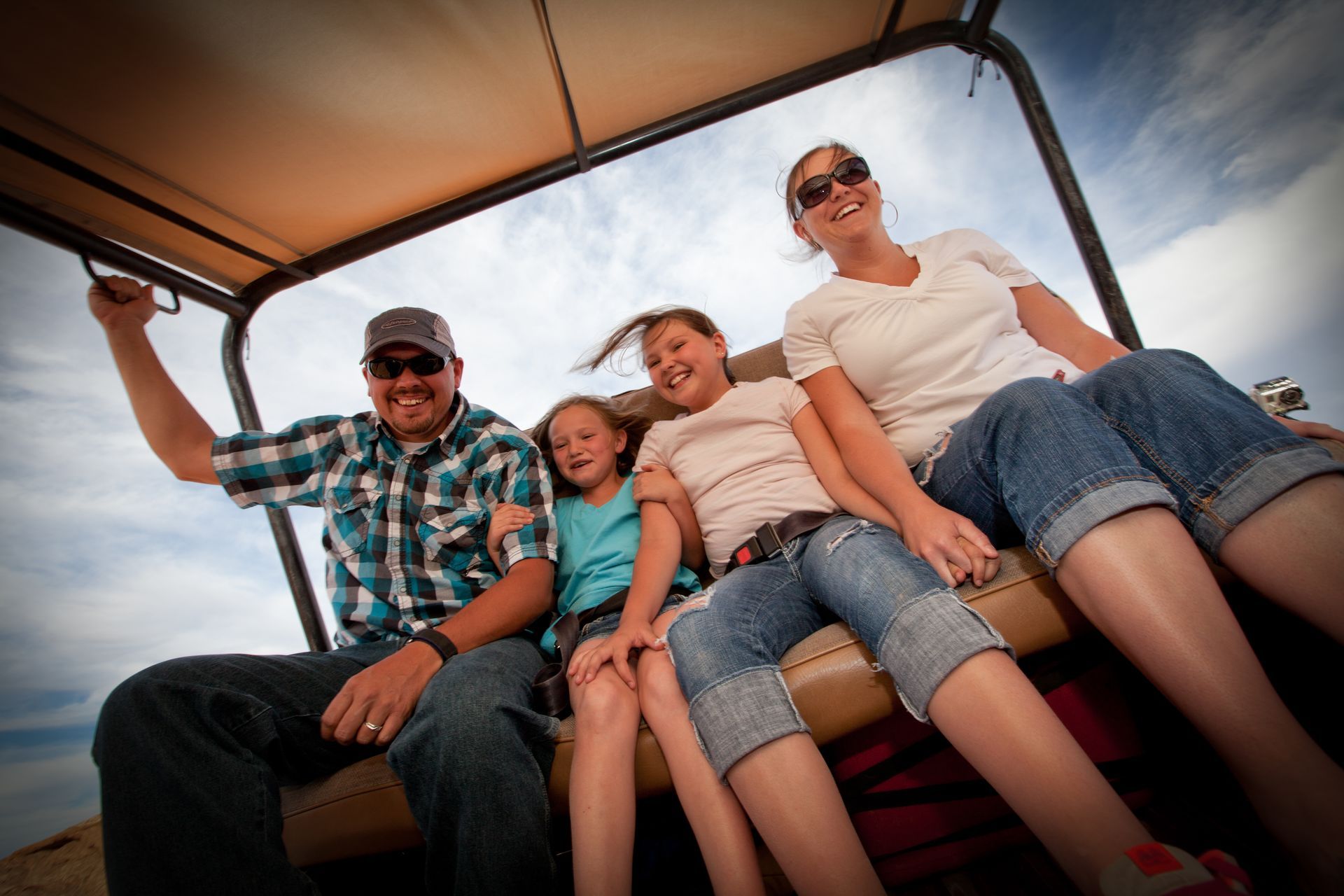 Family in Hummer smiles and arms up, under sunny sky.
