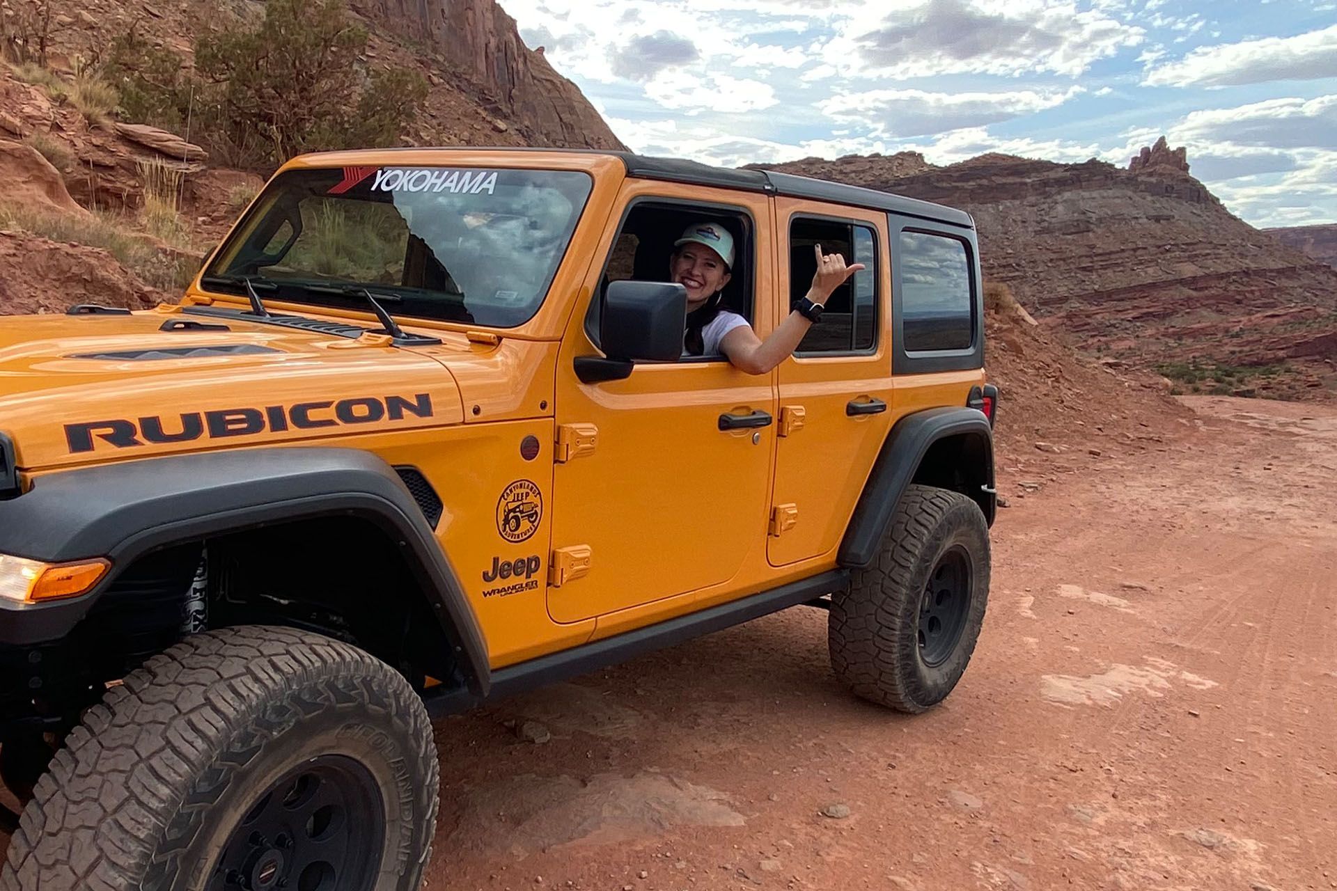 Person in an orange Jeep Rubicon giving a thumbs up in a desert landscape.