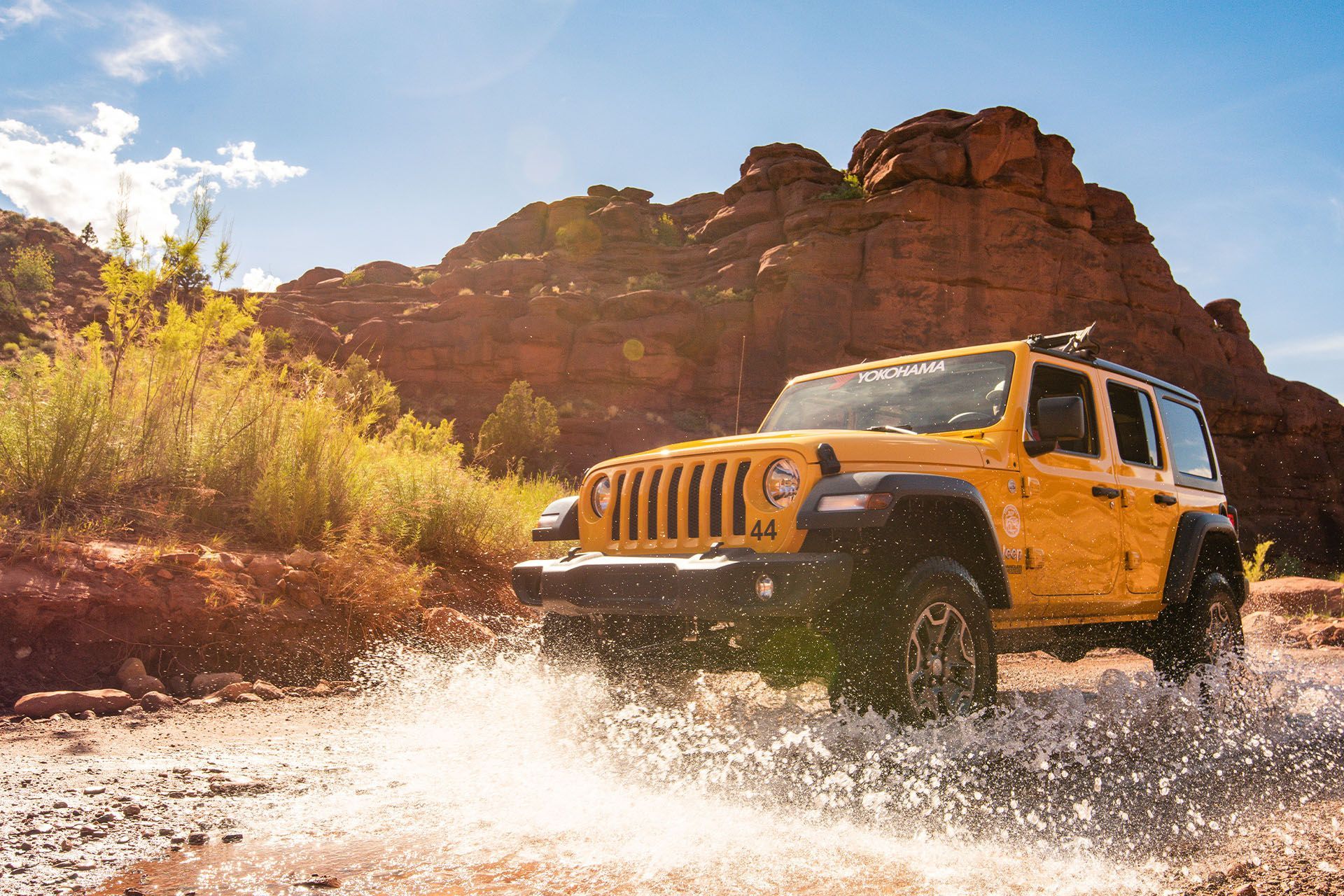A yellow jeep is driving through a river in the desert.