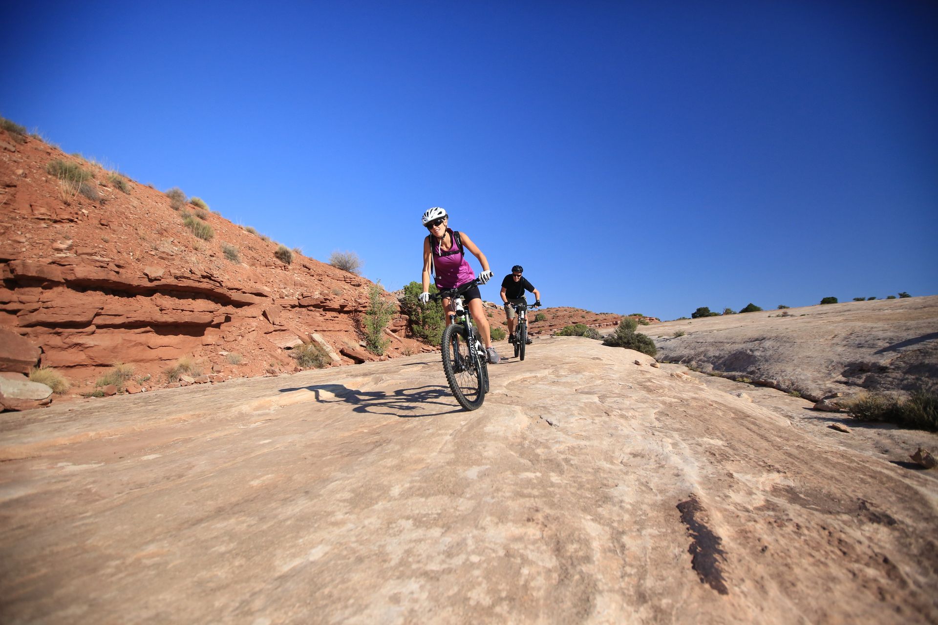 Two mountain bikers ride down slickrock terrain on the Klondike Bluffs Trail in Moab.