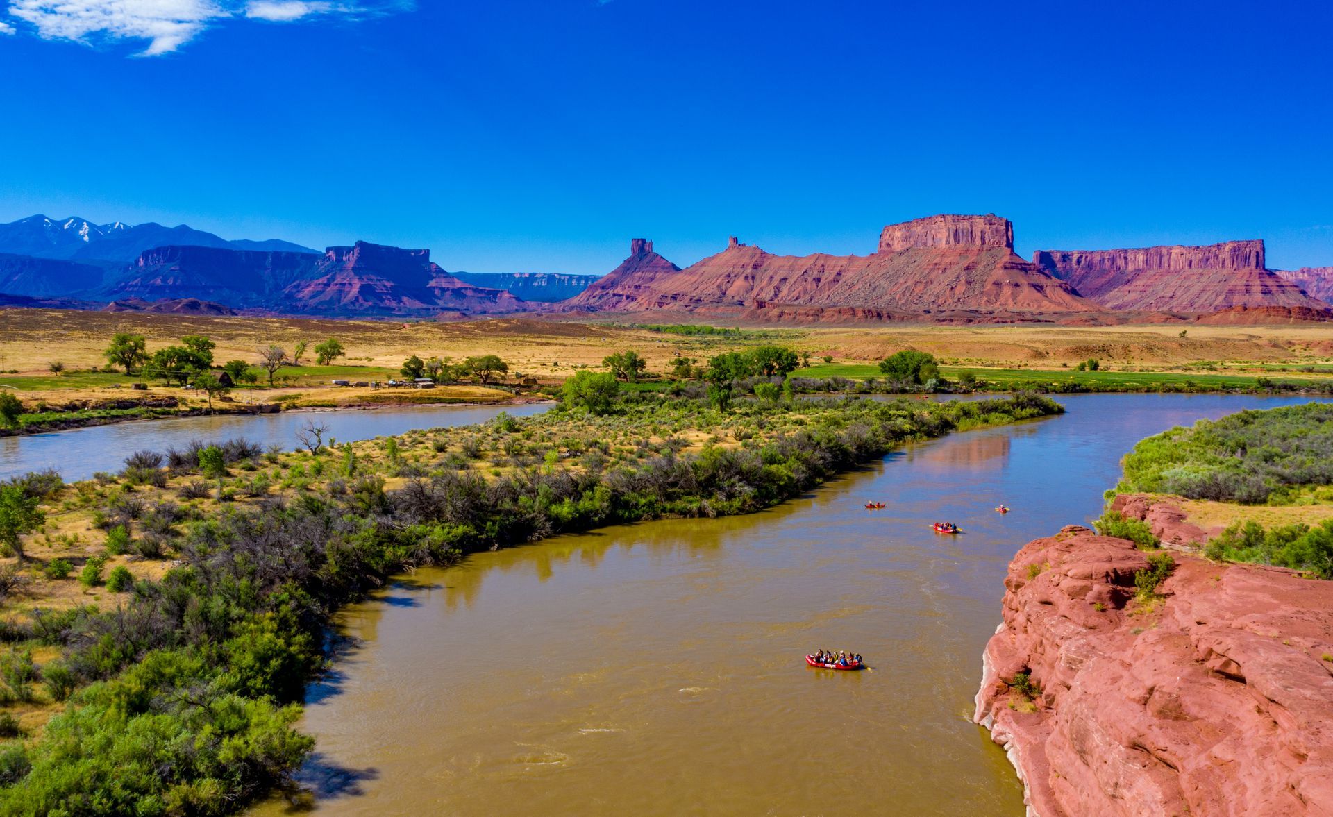 View of the Colorado River winding through Castle Valley with rafts floating on calm water.
