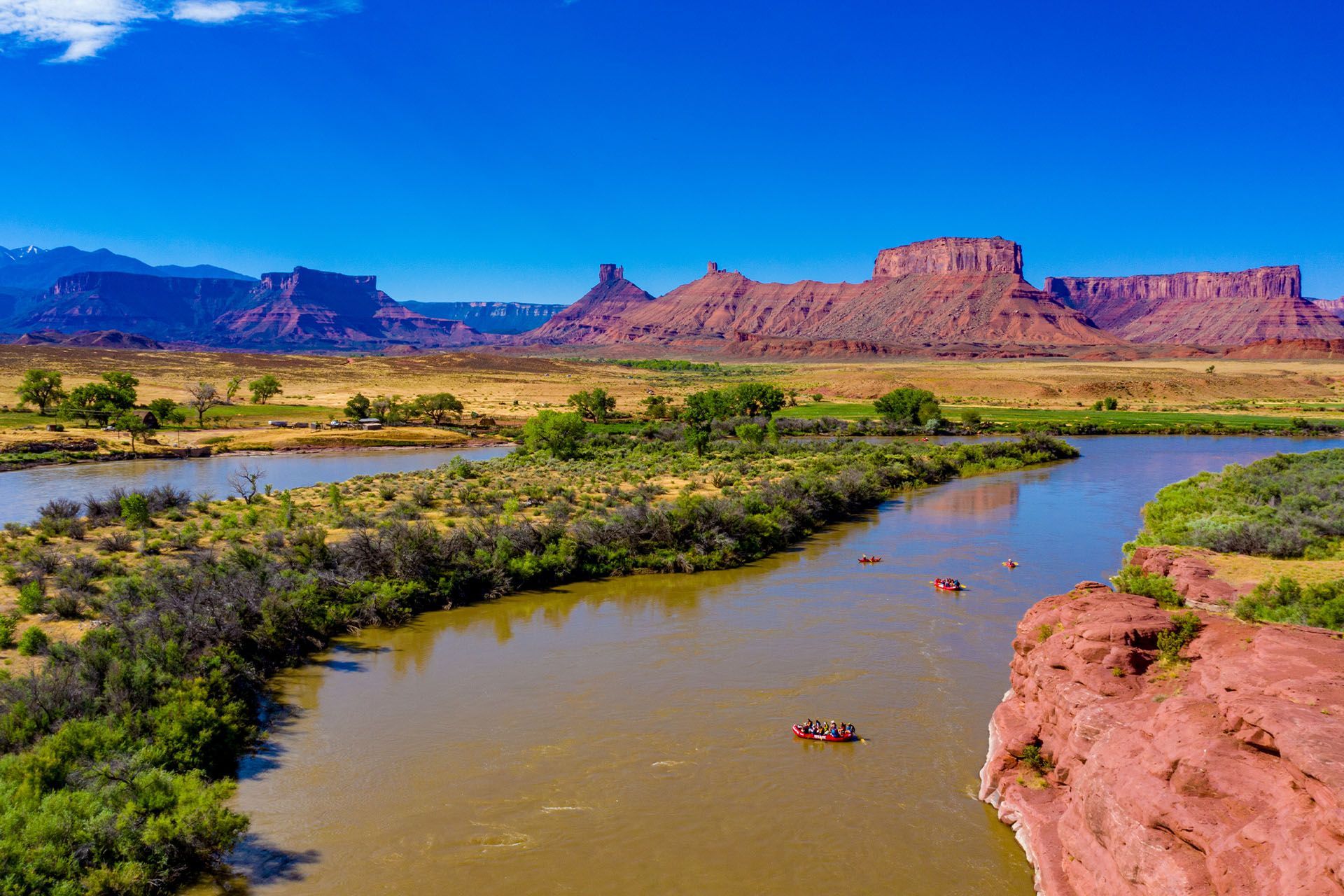 Rafting on a river surrounded by red rock formations in Castle Valley under a clear blue sky.