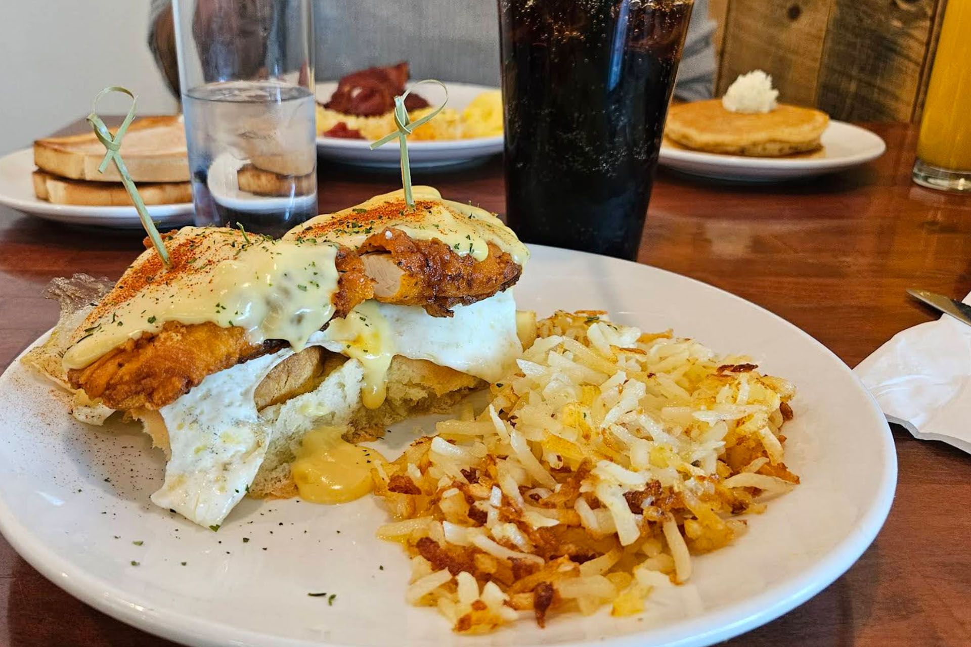 Plate with eggs benedict, hash browns, and drinks on a table.