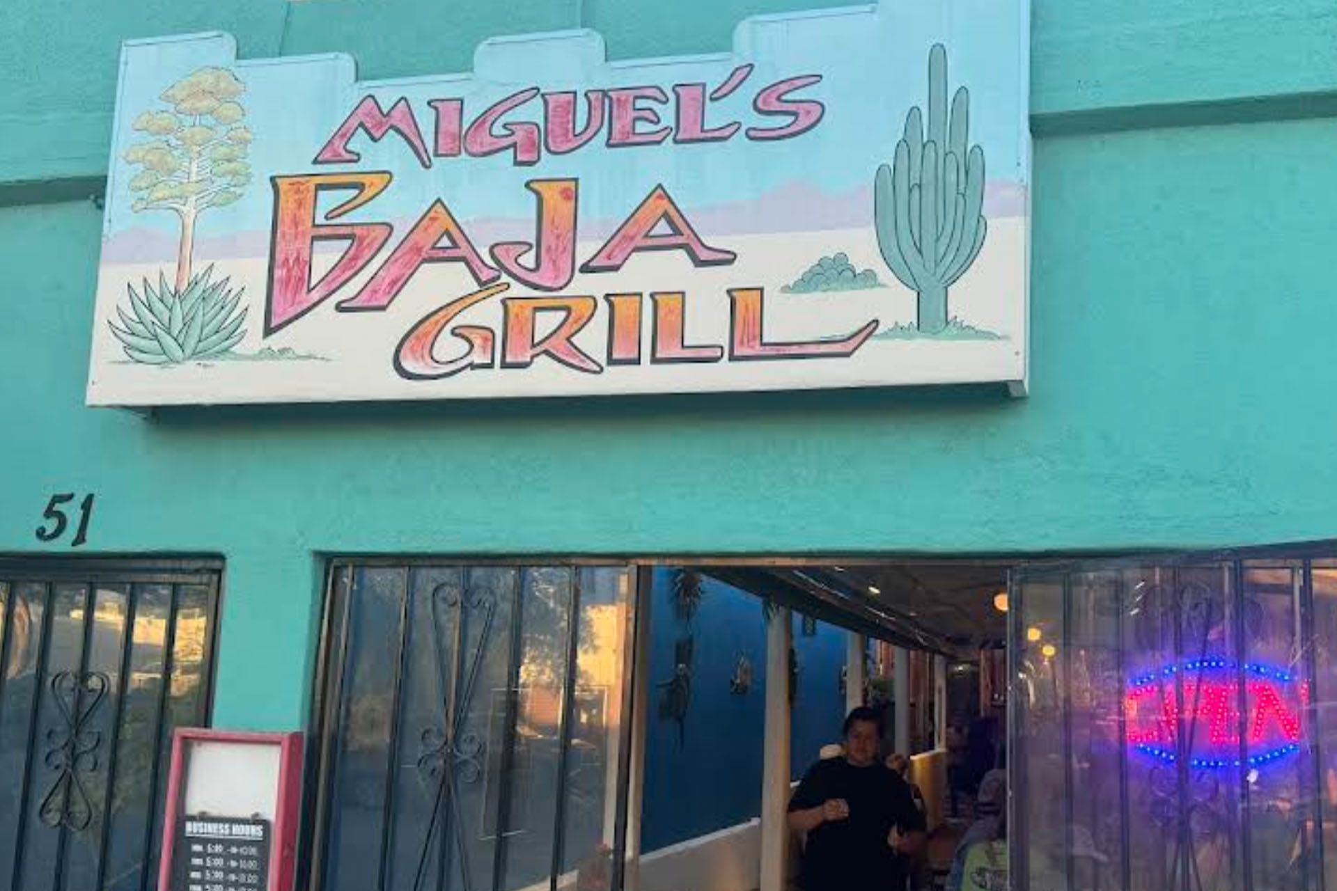 Miguel's Baja Grill restaurant with teal facade, sign, and entrance; person enters.