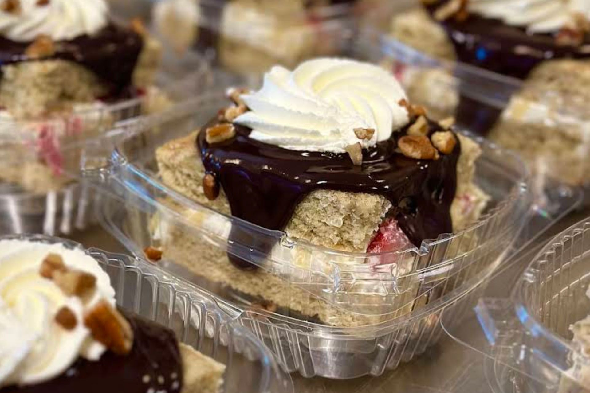 Cake slice with chocolate, whipped cream, and nuts in a clear plastic container.